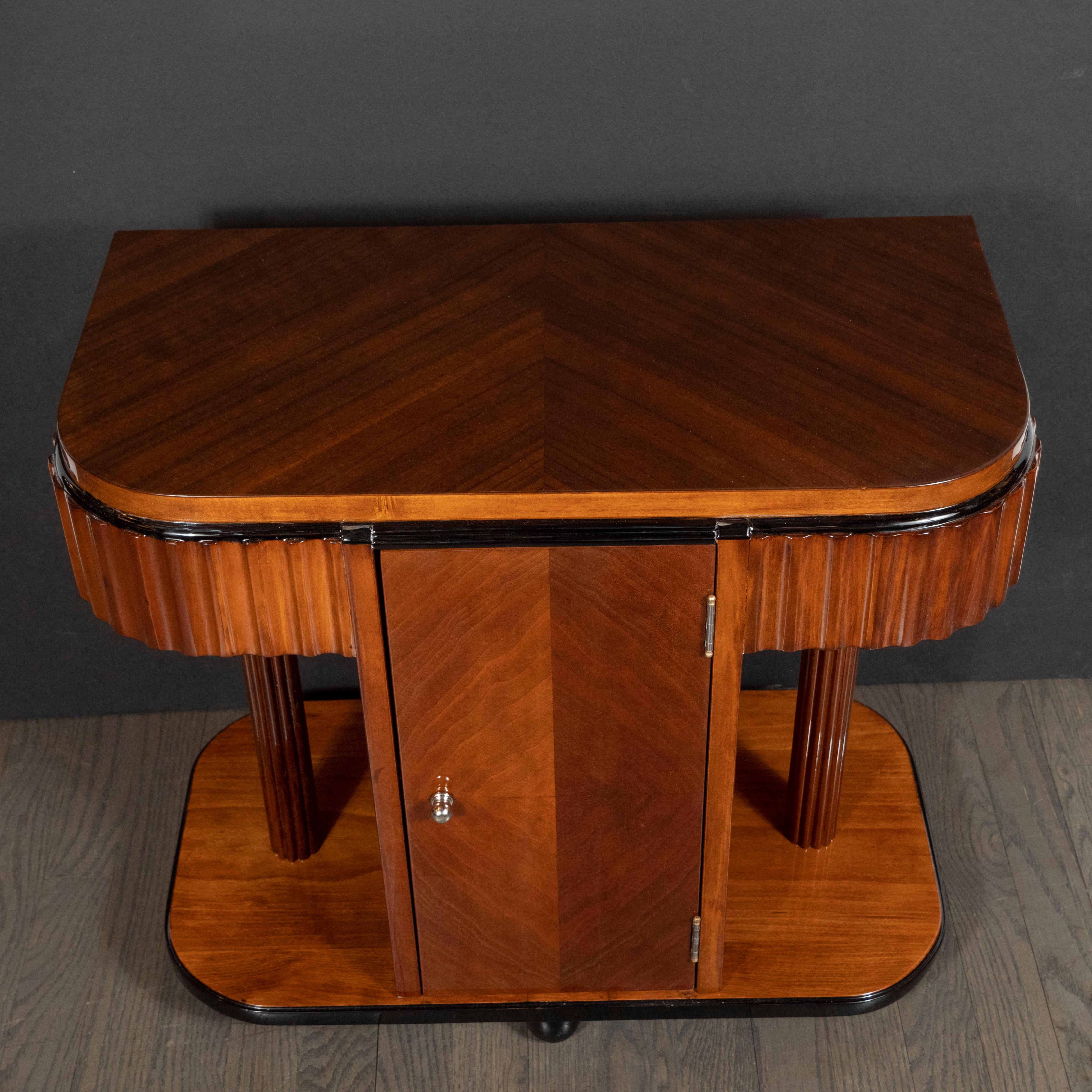 This stunning pair of Art Deco Machine Age end tables or nightstands were realized in the United States circa 1935. They feature skyscraper style walnut tops (with black lacquer banding) whose grain has been bookmatched to create a stunning