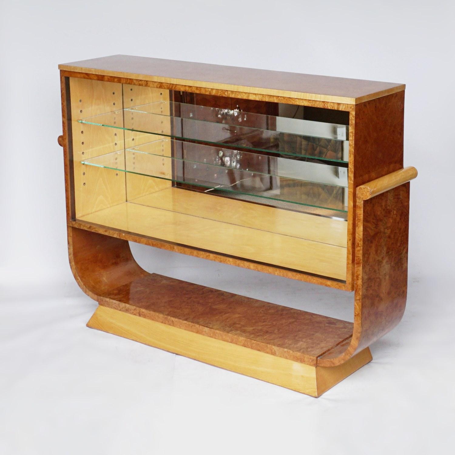 A pair of Art Deco bookcases by Harry & Lou Epstein. Burr walnut and satin birch veneers with a macassar ebony banding. Mirrored lit interior with two glass shelves. Set over a U-shaped base.

Dimensions: H 95cm, W 130cm, D 32cm

Origin: