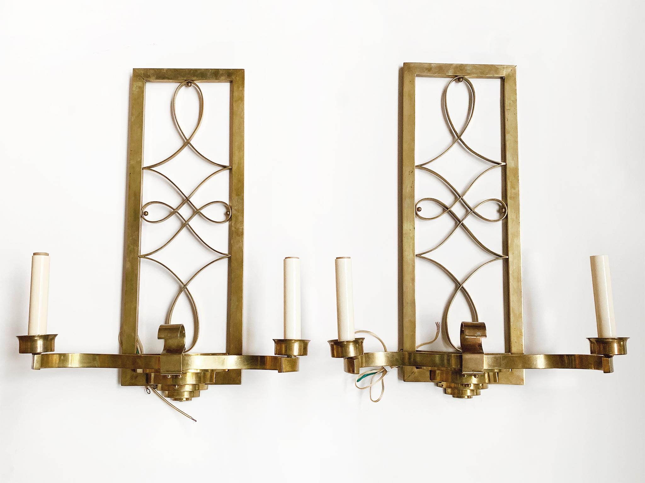 An elegant pair of Art Deco brass sconces, early 20th century. The back frame is designed with a whimsical curlicue motif that creates a lattice. Two arms curve outward and culminate into candle-style sockets. The sconces are newly rewired and