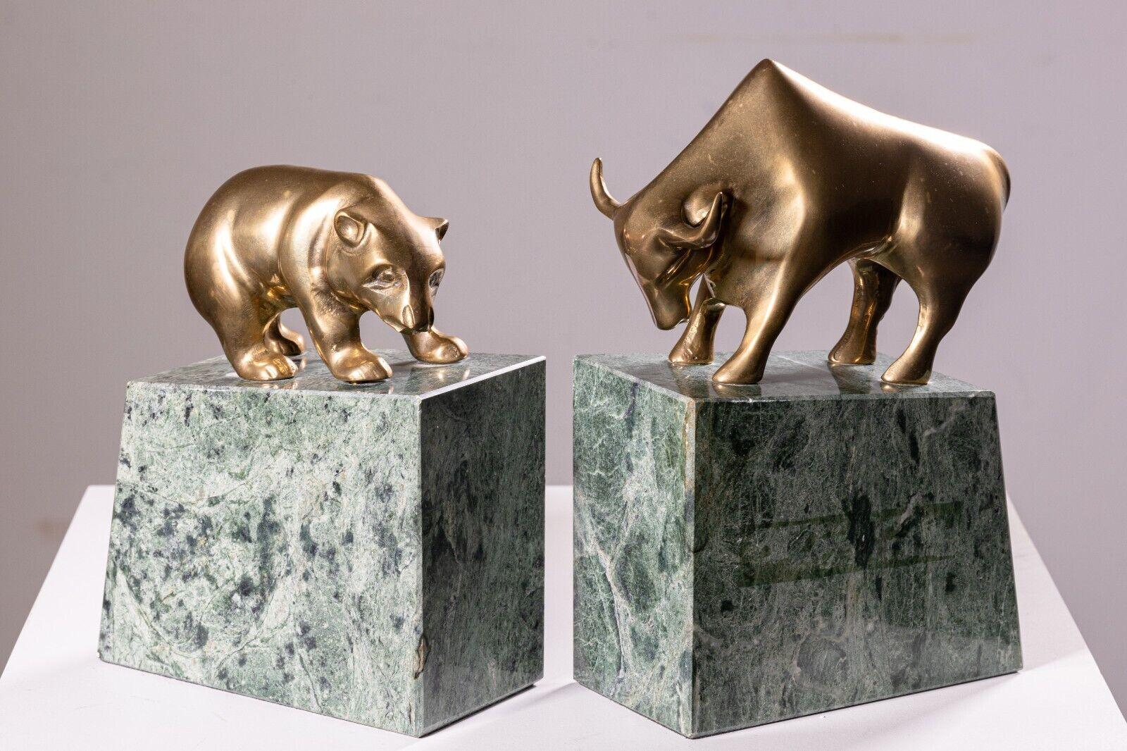 A pair of art deco brass bull and bear bookends. These lovely bookends feature a green marbled stone construction with a felt bottom, and a brass animal sculpture top. Each sculpture, the bull and bear, and very detailed and lively. These pieces are