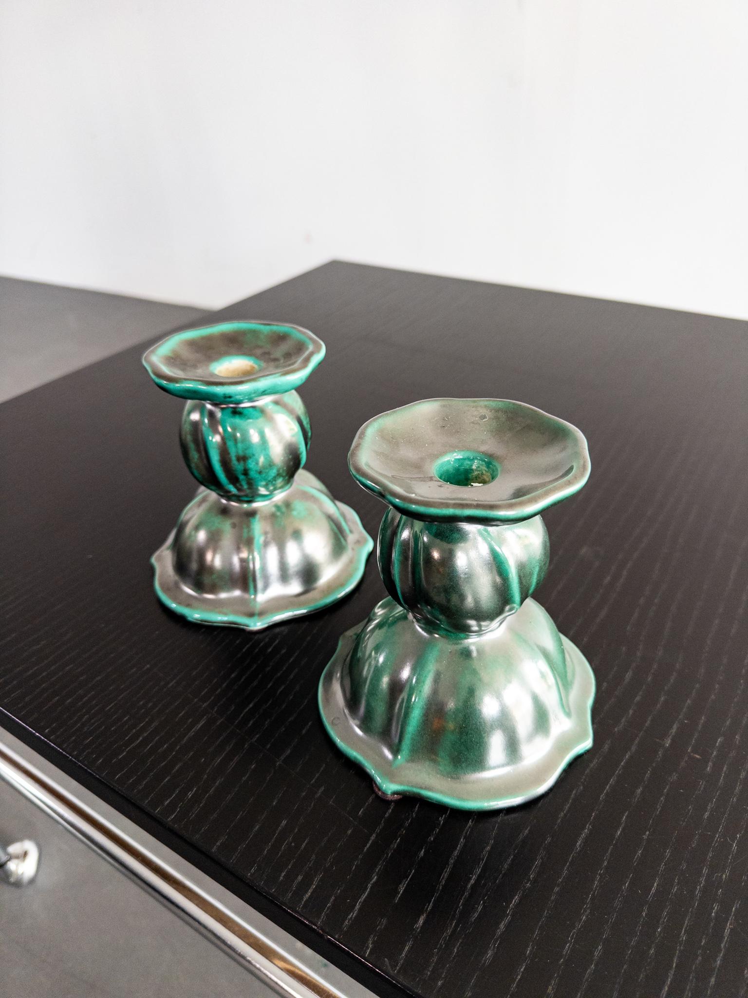 Una rara e sorprendente coppia di candelieri in ceramica del rinomato produttore svedese Upsala Ekeby. Risalenti agli anni '30, questi pezzi scultorei incarnano l'eleganza dell'epoca Art Déco con la loro silhouette voluttuosa e lo smalto verde
