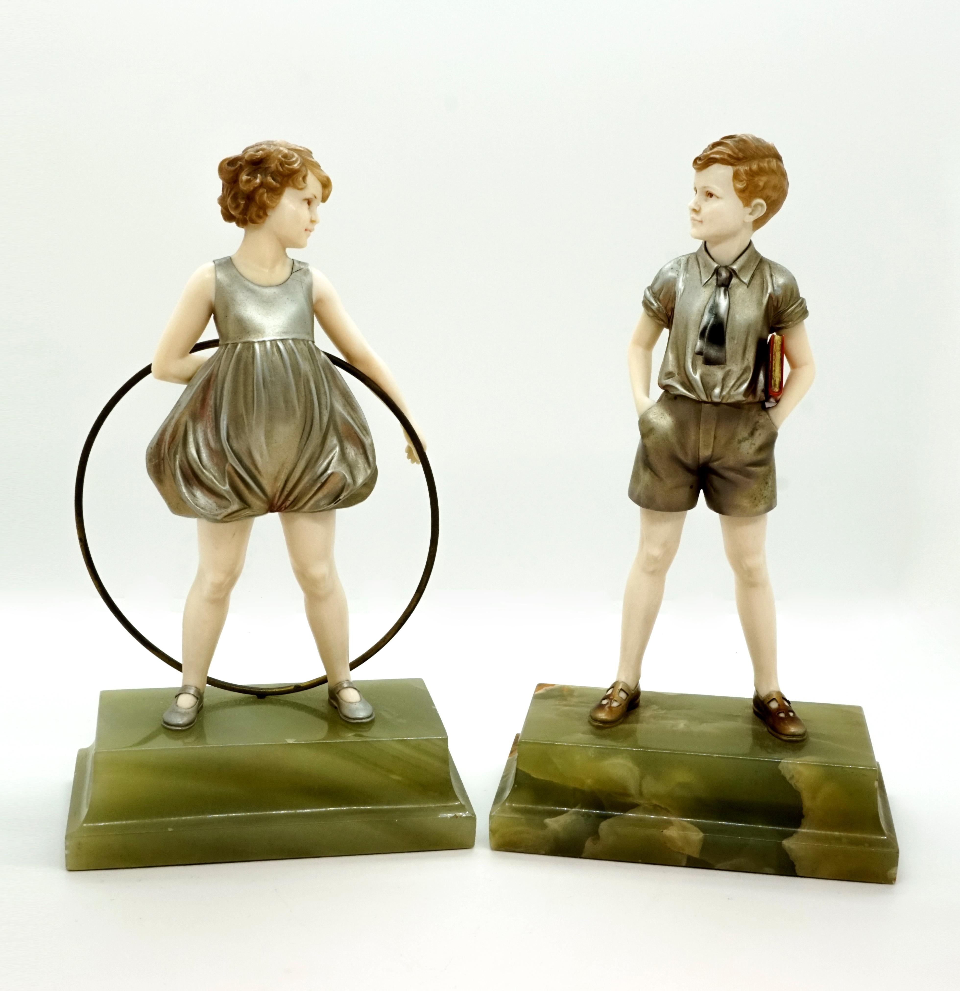 Two dainty, finely crafted children's figures:
Schoolboy with a book under his arm, his hands loosely tucked into his pockets and 
young girl in play jersey, holding a large hoop and stick behind her.
The bare body parts carved out of bone,