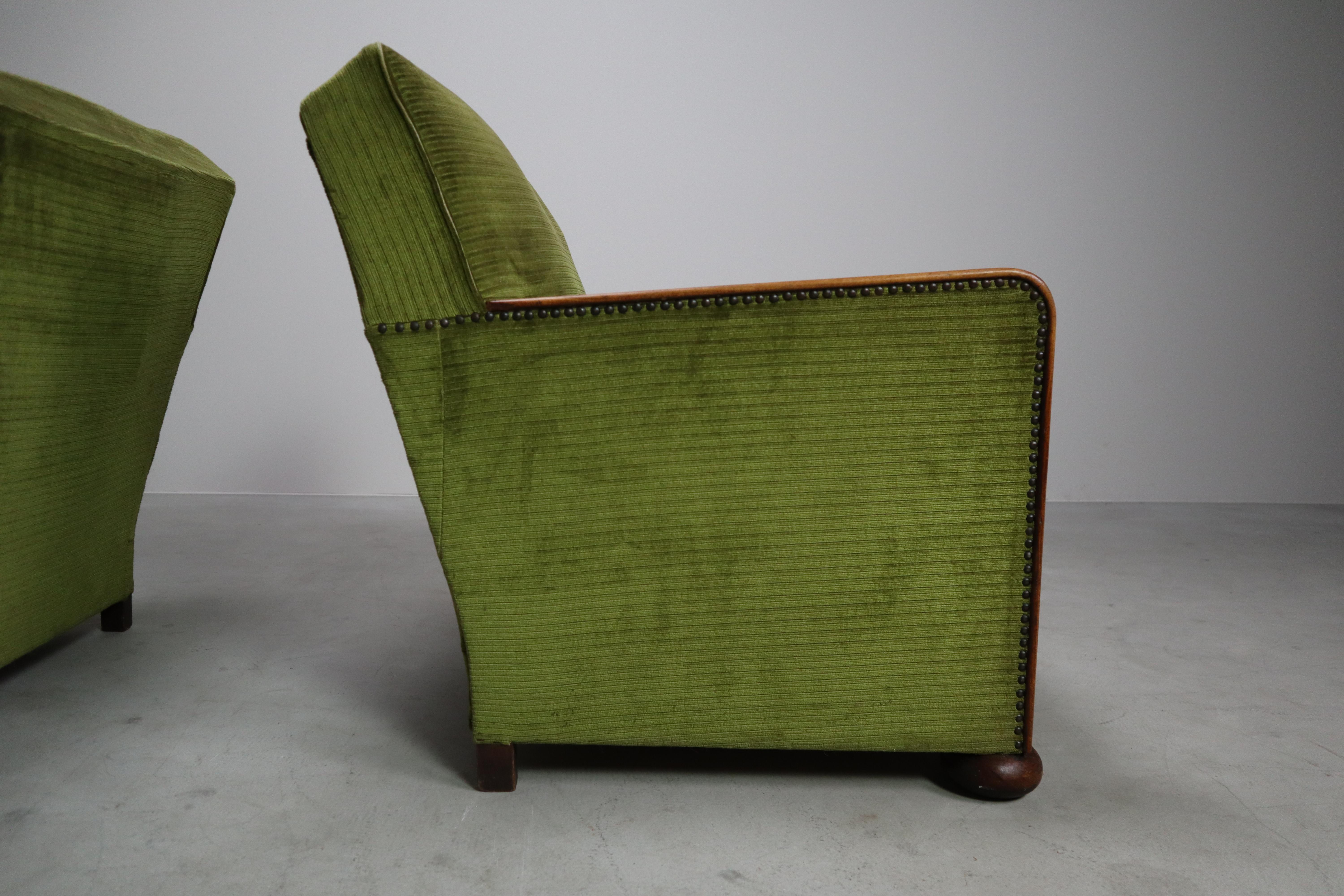 Una raffinata coppia di autentiche sedie da club Art Déco, circa 1930. Le sedie presentano braccioli in legno massiccio con curve eleganti, piedi corti e arrotondati e borchie decorative lungo i bordi. Rivestiti con il probabile velluto a coste