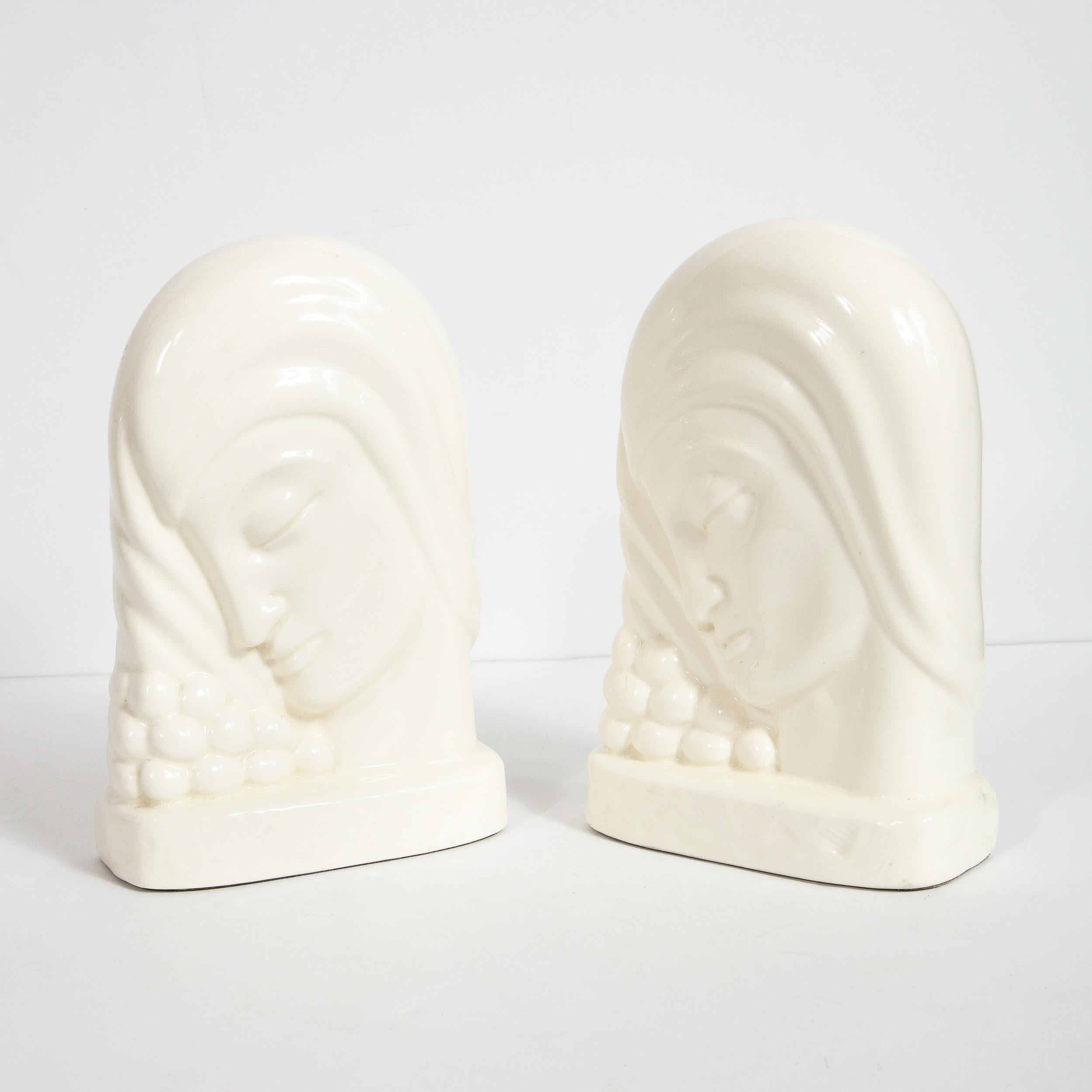 This elegant pair of Art Deco book ends were realized by the esteemed Art Deco maker Kent Art Ware in Japan, circa 1930. They feature a stylized female figure with her eye closed, her head slightly askew, resting on a collection of spherical forms,