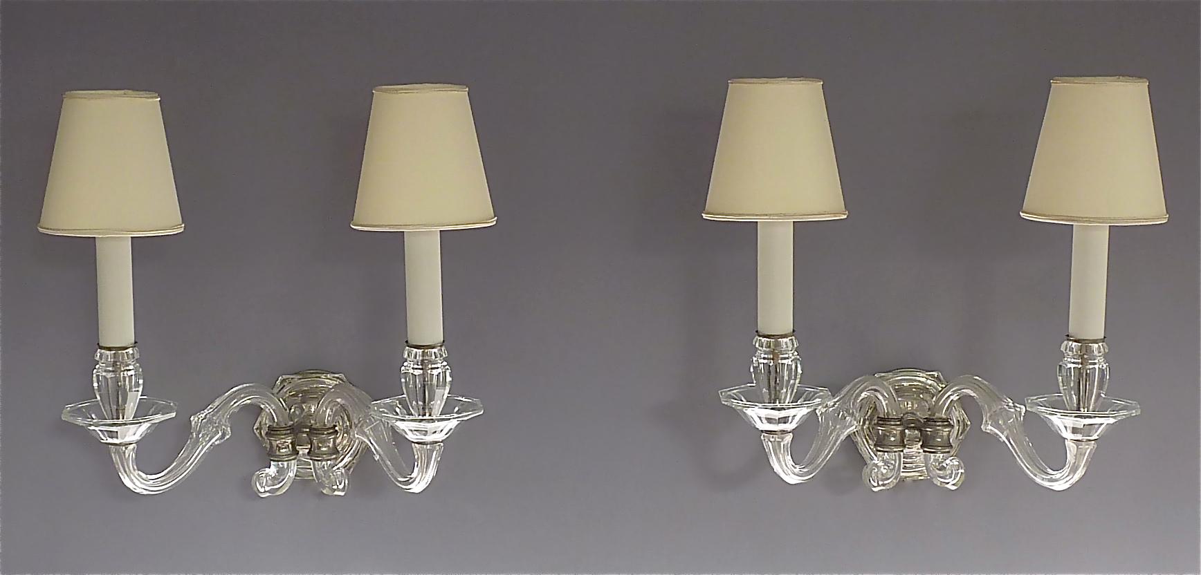 Preziosa coppia di appliques o lampade da parete in cristallo sfaccettato tagliato a mano a 2 bracci in stile Art Déco classico, con paralumi bianchi off, nello stile di Baccarat, Francia o Germania, 1920-30 circa. Le bellissime applique in vetro