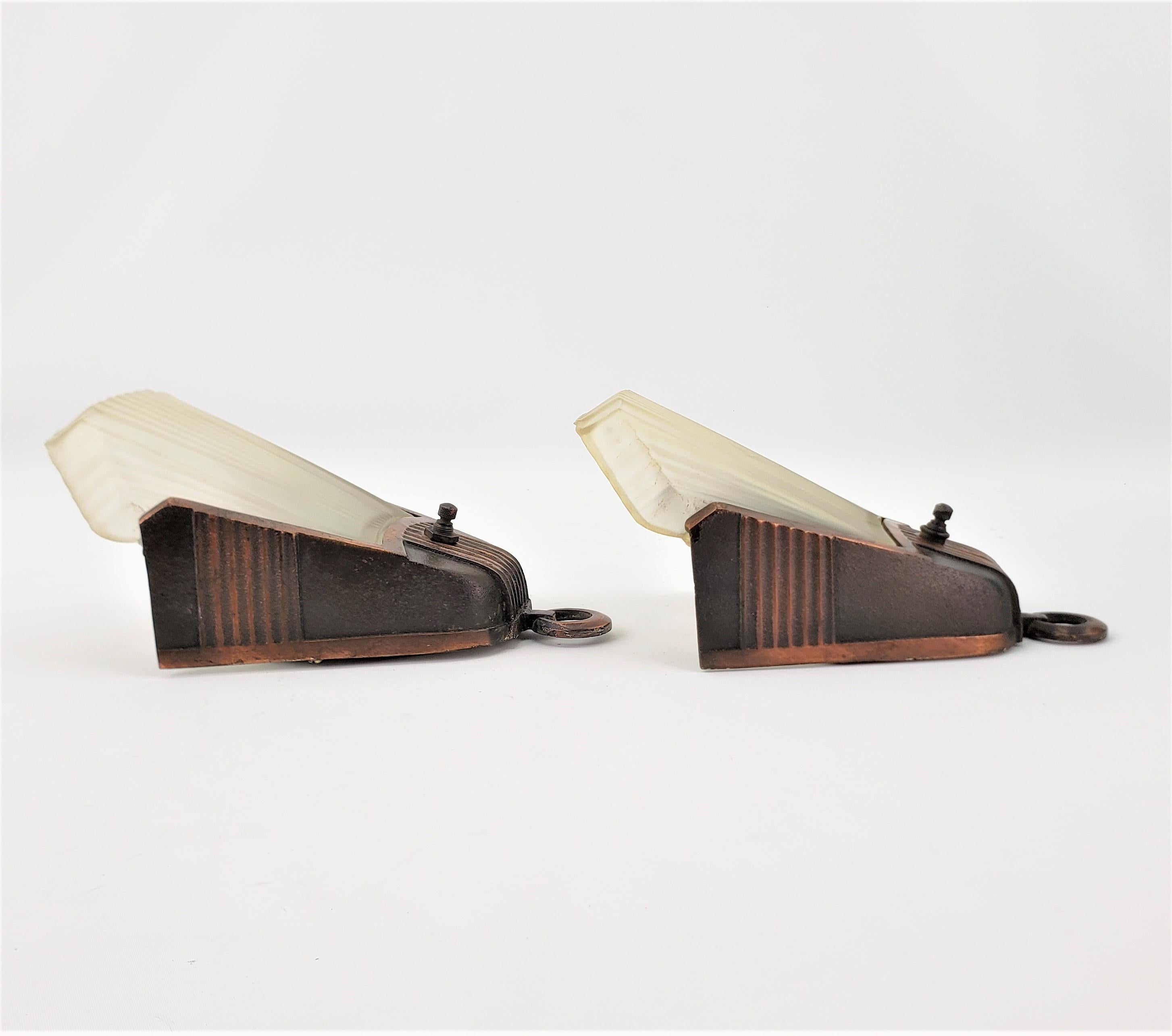 This pair of Art Deco frosted glass slip shade wall sconces are unsigned, but presumed to have been made in the United States in approximately 1920 in the period Deco style. The wall brackets are made of metal with a brass or bronze patination, and