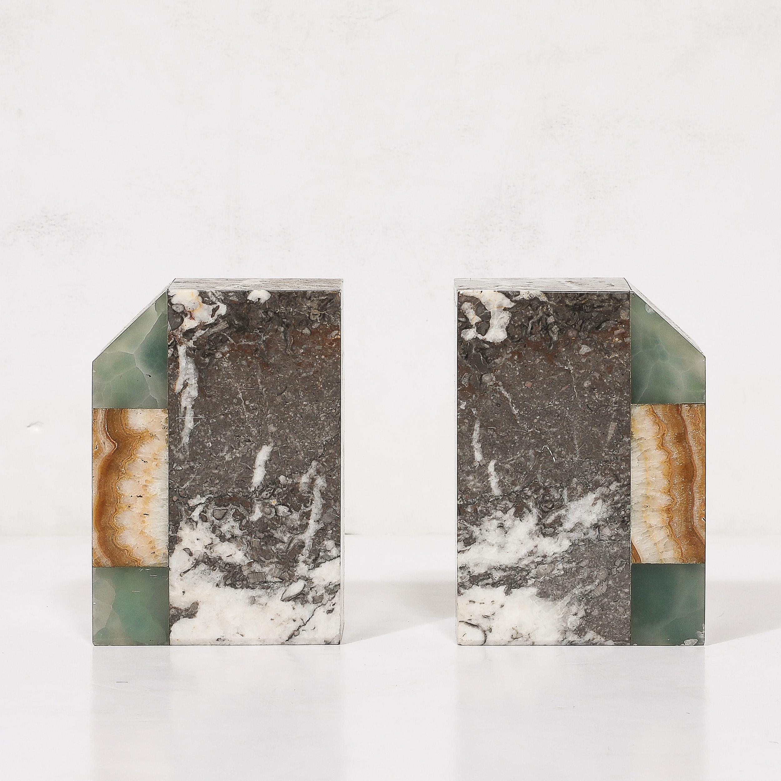 Questa elegante coppia di fermalibri Art Déco, realizzati in Francia intorno al 1930, combina materiali pregiati e geometrie audaci. Caratterizzati dal marmo esotico Nero Marquina grigio e da due tipi di onice - verde brillante e marrone ricco -