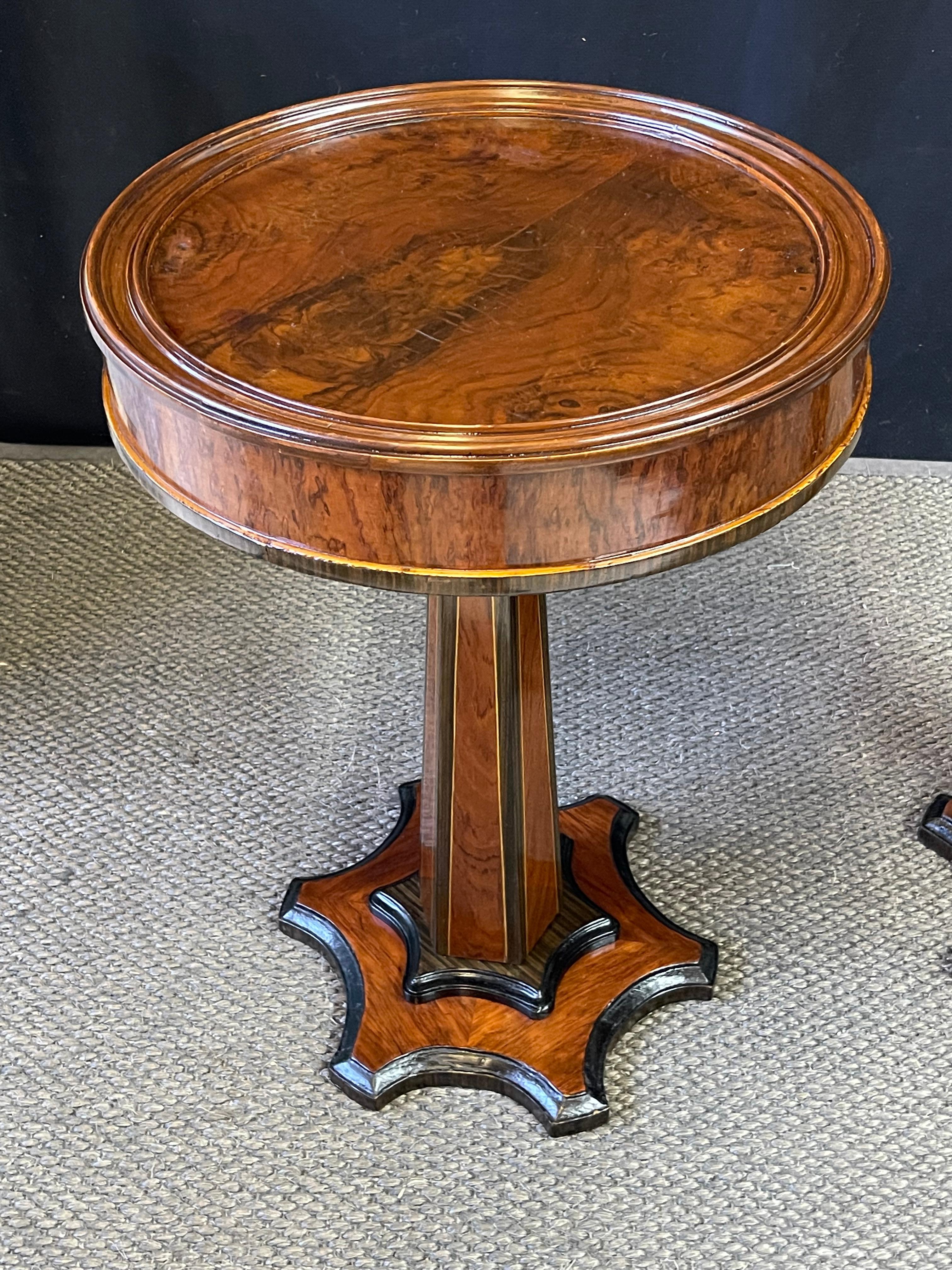 This is a striking pair of early 20th Century French Art Deco gueridon tables rich in burled wood veneers of walnut and palisander with intricate satinwood inlay and ebonized accents. Each circular table top is inset in a molded gallery above a
