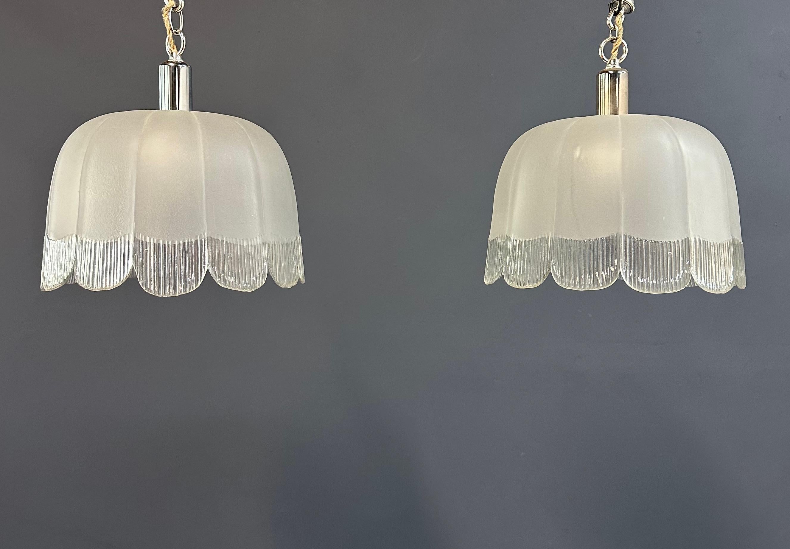 A refined pair of Art Deco hand-blown glass pendant shades, circa 1930s. Each shade is crafted with softly frosted glass, accented by scalloped edges and clear ribbed detailing that catch the light with subtle brilliance. The fluid petal-like form