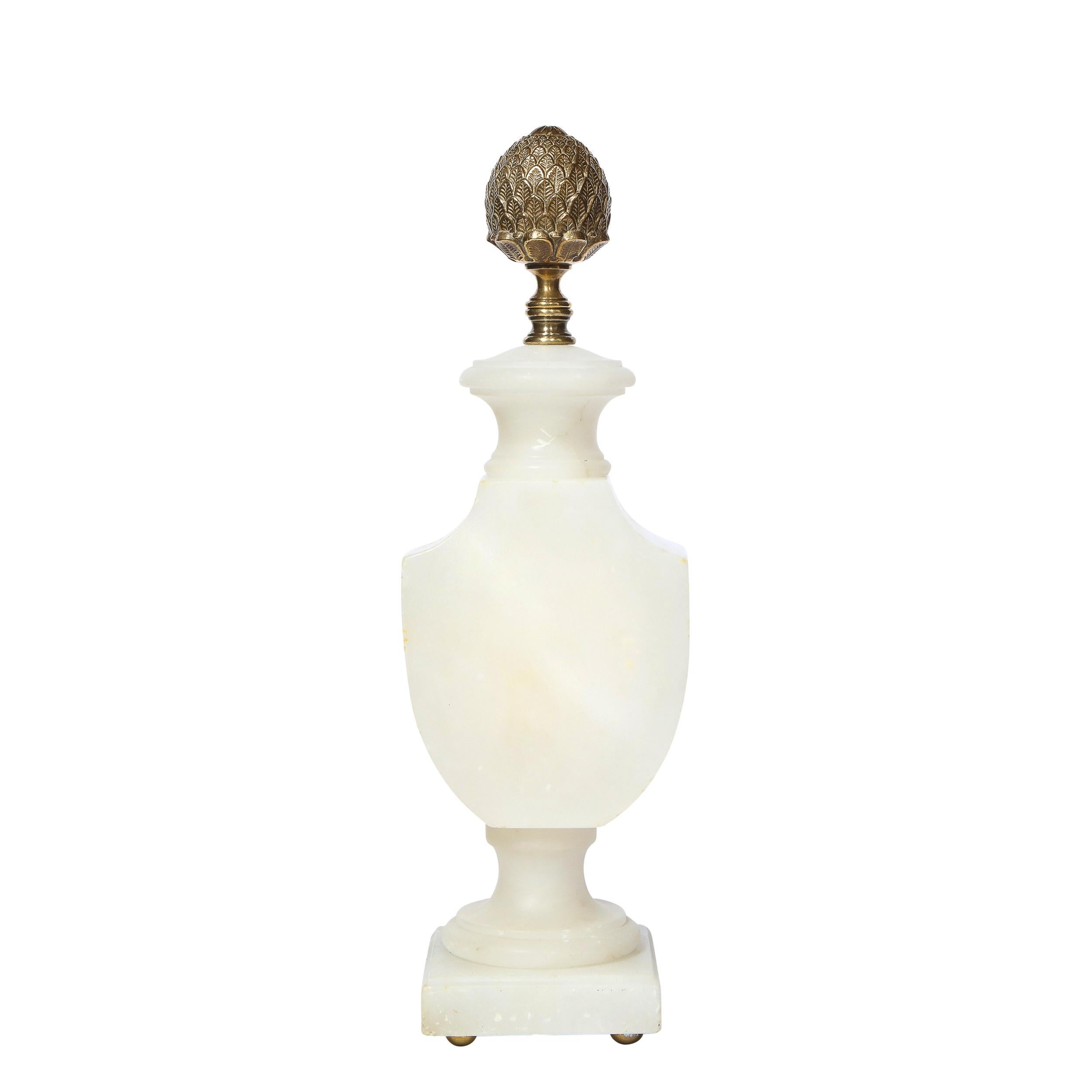 This gorgeous pair of 1940s Hollywood Art Deco table lamps were realized in France, circa 1940. They offer sculptural carved alabaster stylized urn form bodies that are illuminated from within crowned with bronze pommes de pin finials. With their