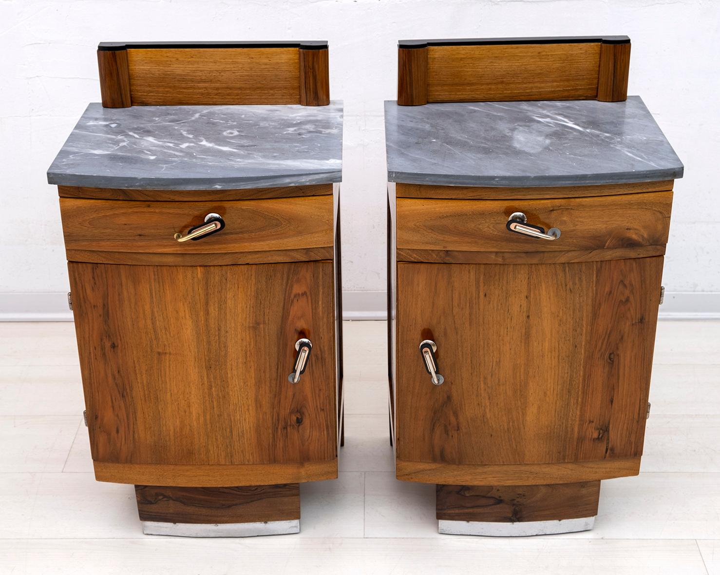 This pair of bedside tables was produced in Italy in the 1920s, Art Deco period. They were made of solid European walnut, the top is in graphite gray marble, the structure is in poplar and the handles are in brass and Bakelite. The band below is in