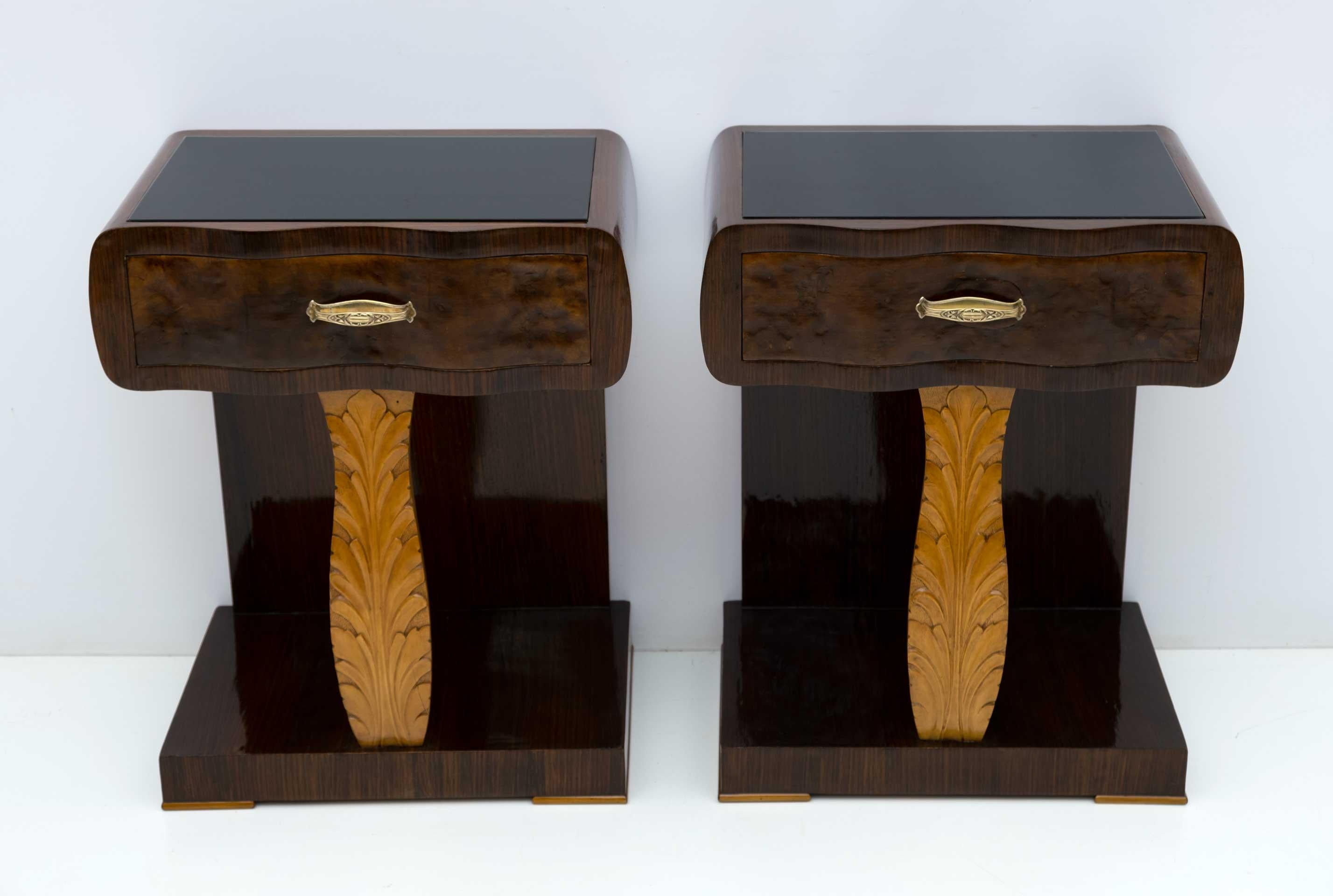 This pair of bedside tables was produced in Italy in the 1920s, Art Deco period. They were made in striped walnut, walnut briar and maple, the top is in black painted glass, the structure is in poplar, the handles in brass. They have been completely