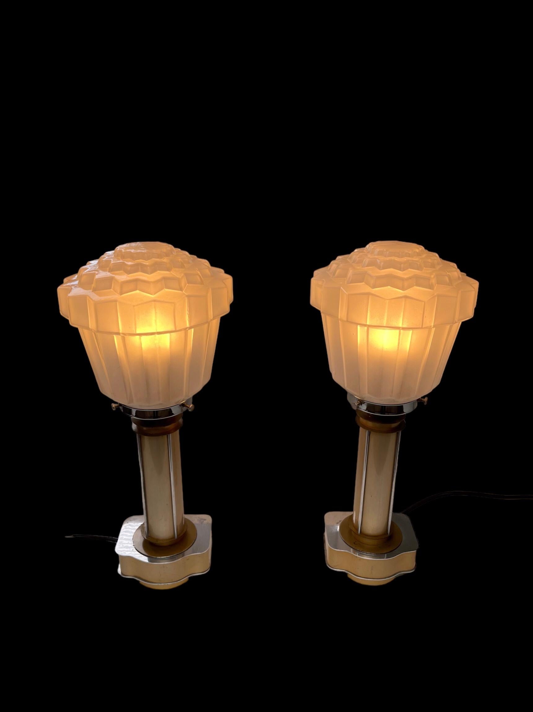 A pair of unusual, yet stylish Art Deco lamps with gold anodised aluminium pedestals and aluminium and gold painted bases. Some wear to the gold painted bases, commensurate with age, as photographed. 
With attractive fluted, stepped glass shades.