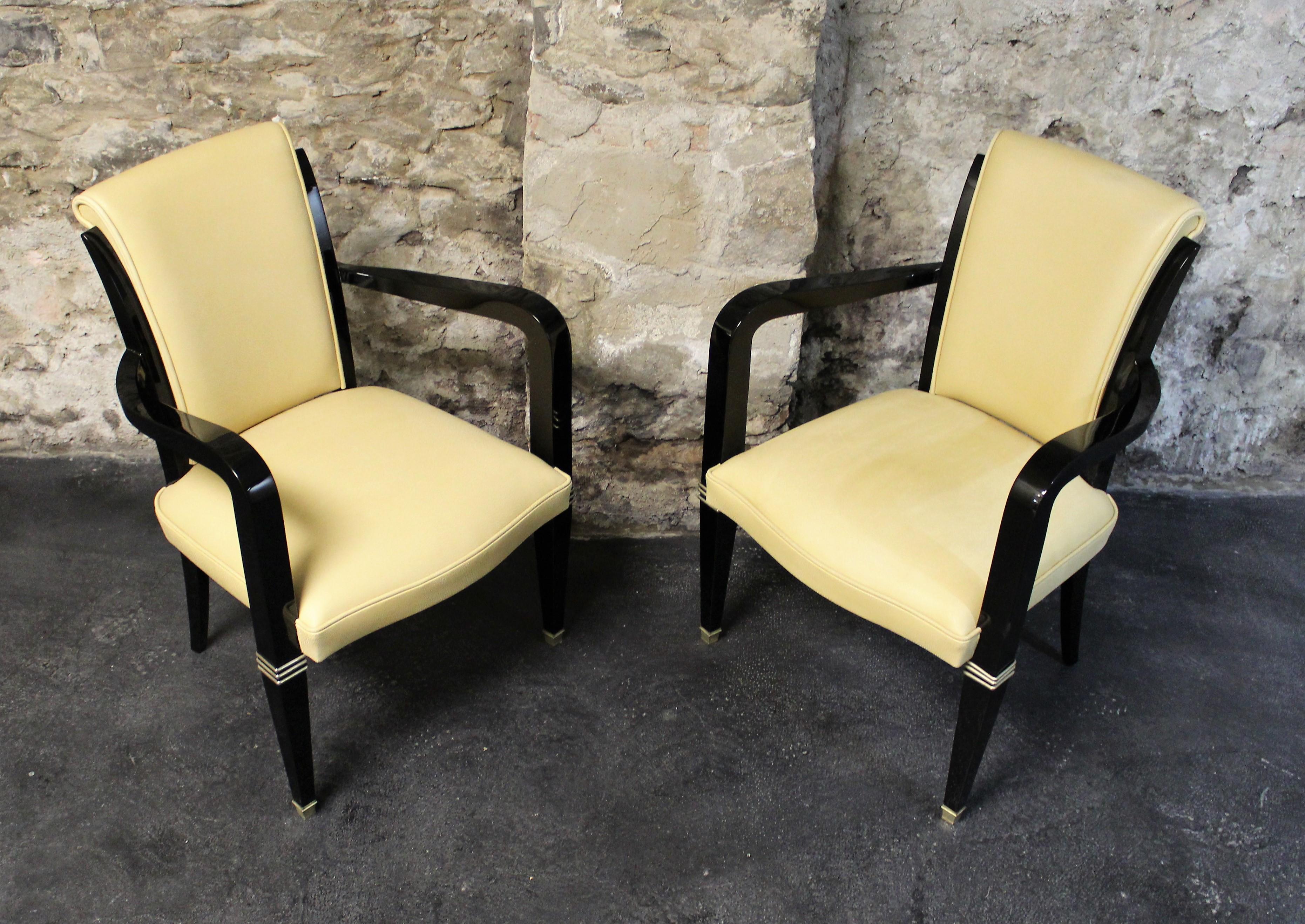 Pair of Art Deco polished ebonized frame armchairs with chrome accents and cream leather upholstery.