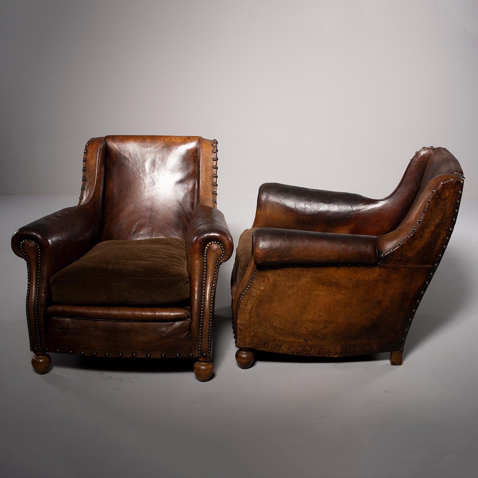Pair of French leather club chairs with wood frames. Chairs feature subtle side wings, rolled arms, exposed wood frames, brass nailhead trim and bun feet. Original dark brown leather upholstery with newly upholstered brown alpaca velvet seat