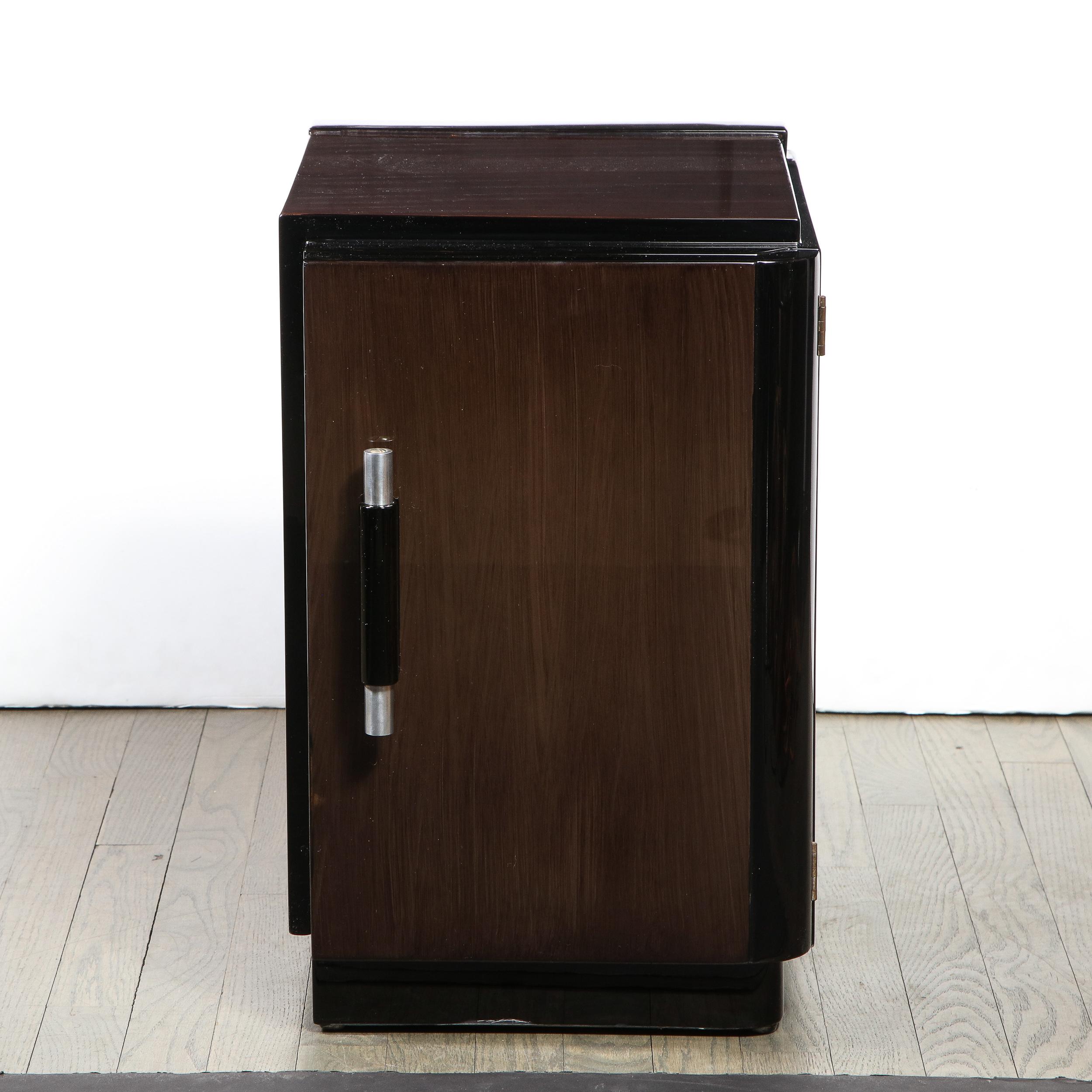 This graphic and elegant pair of Art Deco Machine Age nightstands were realized in the United States circa 1935. They feature rectilinear bodies with stepped skyscraper style bases; black lacquer detailing circumscribing the edges; and streamlined