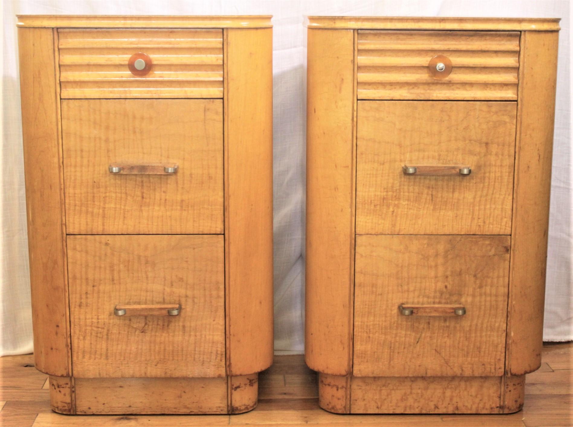 This matched pair of commodes are unsigned, but presumed to have been made in the United States in approximately 1925 in the period Art Deco style. These nightstands or cabinets have a streamlined shape and accenting top drawer and covered in a