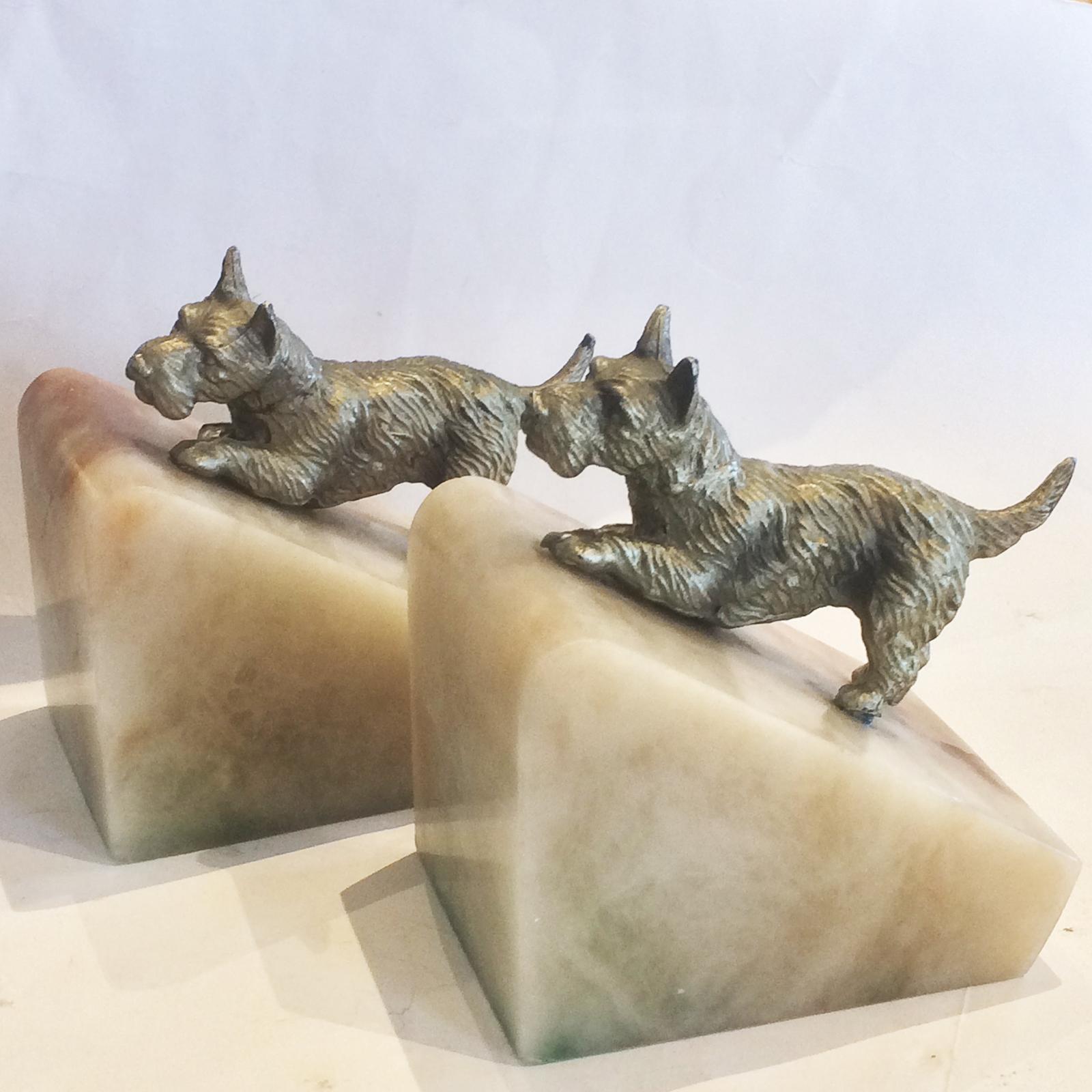Art Deco pair of bookends having Scottie Scottish Terriers on colored alabaster of cream, brown and green. Both are in excellent condition with no repairs, and they have the original felted paper to the base for to assist protect the surface they