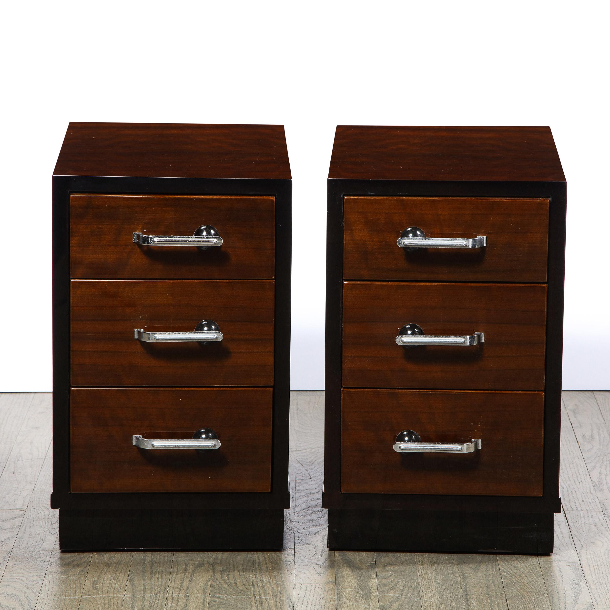 This stunning pair of Machine Age bookmatched walnut and black lacquer nightstands were realized in the United States circa 1935. They feature volumetric rectangular bodies with three drawers framed in black lacquer- all crafted in bookmatched