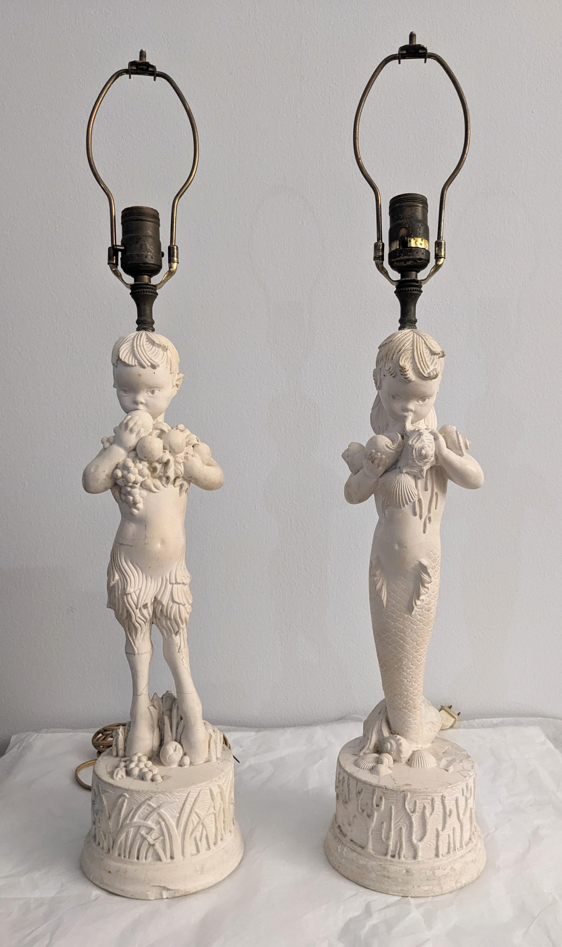 Pair of Charming Art Deco Plaster Surrealist Figural Lamps circa 1940's. Charming Pan and Mermaid figures are molded in plaster.  Pan is carrying fruit set on a base of grass and the mermaid is carrying shells set on coral base. 
There are requisite