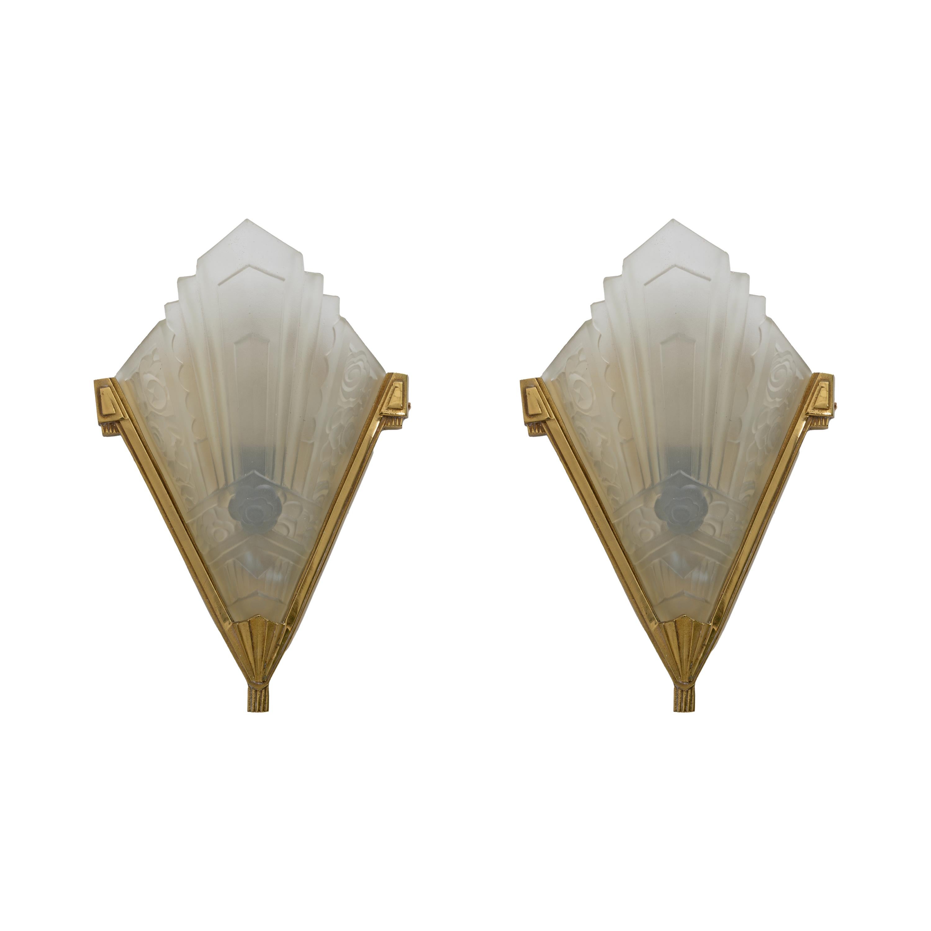Pair of Art Deco wall lamps, France, c. 1930, lampshades in clear glass pressed into a mold and etched, the glasses have geometric and floral motifs, brass structure. 
The lamps have been rewired to US and European standards with lamp holders with