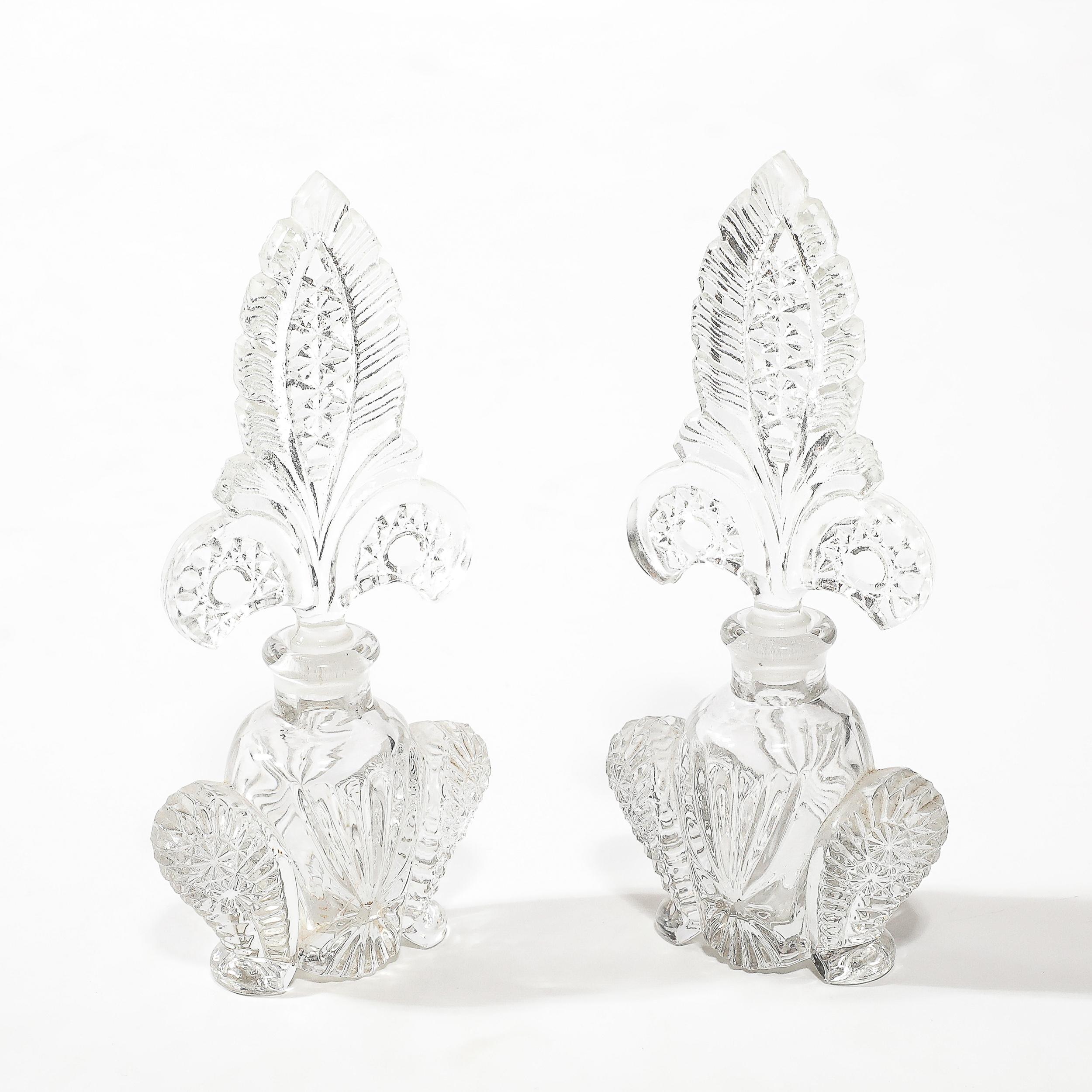 Questa elegante coppia di portaprofumi Art Déco mette in mostra la bellezza senza tempo dell'artigianato del vetro pressato, originario della Cecoslovacchia del 1935 circa. Le bottiglie presentano una sofisticata silhouette geometrica, emblematica