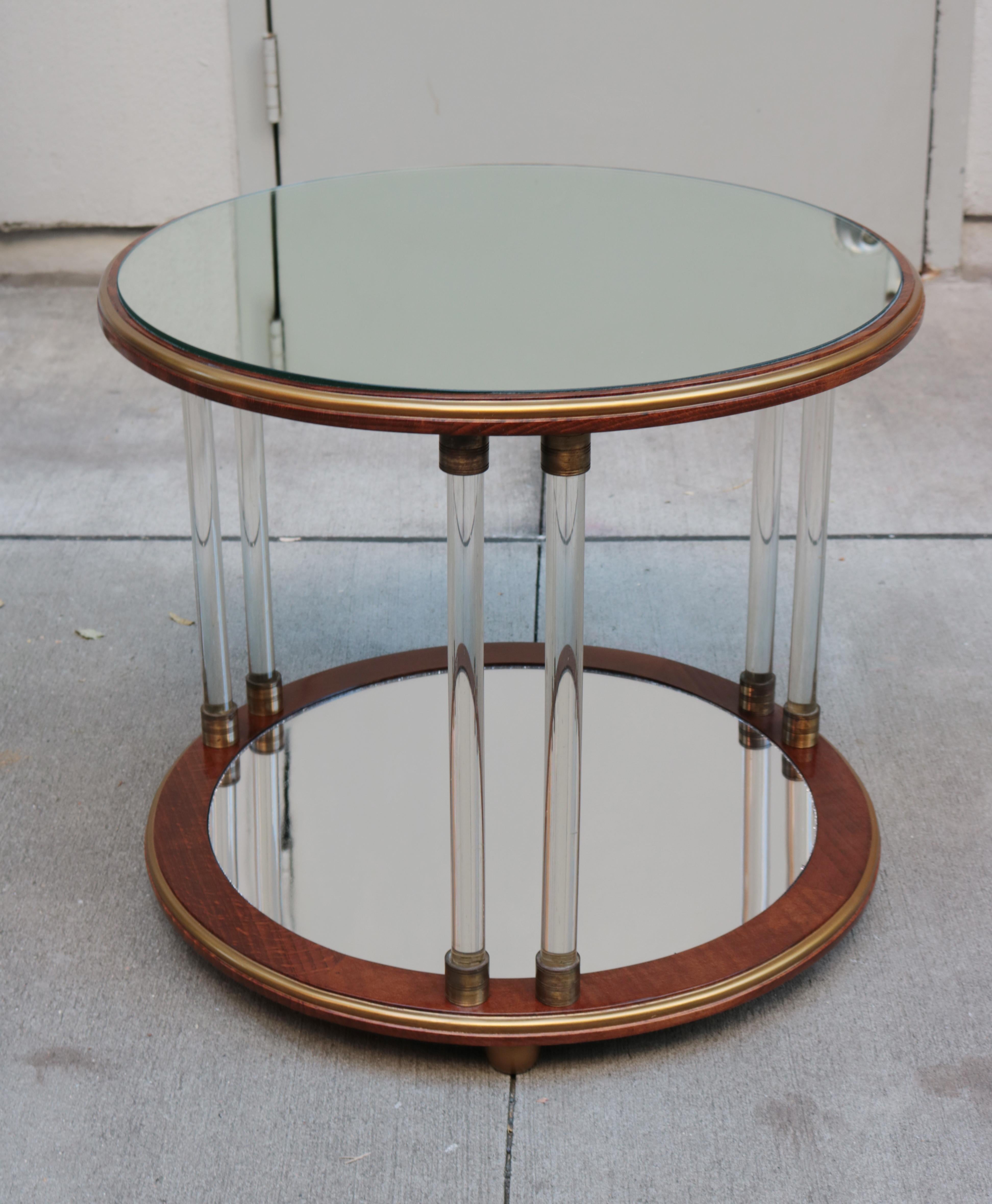 A pair of Art Deco round two-tier side tables. Mahogany with a pair of Art Deco two-tier round side tables. Mahogany with mirror glass tops, glass legs, patinated brass details, giltwood feet and mirrored bottom tier.