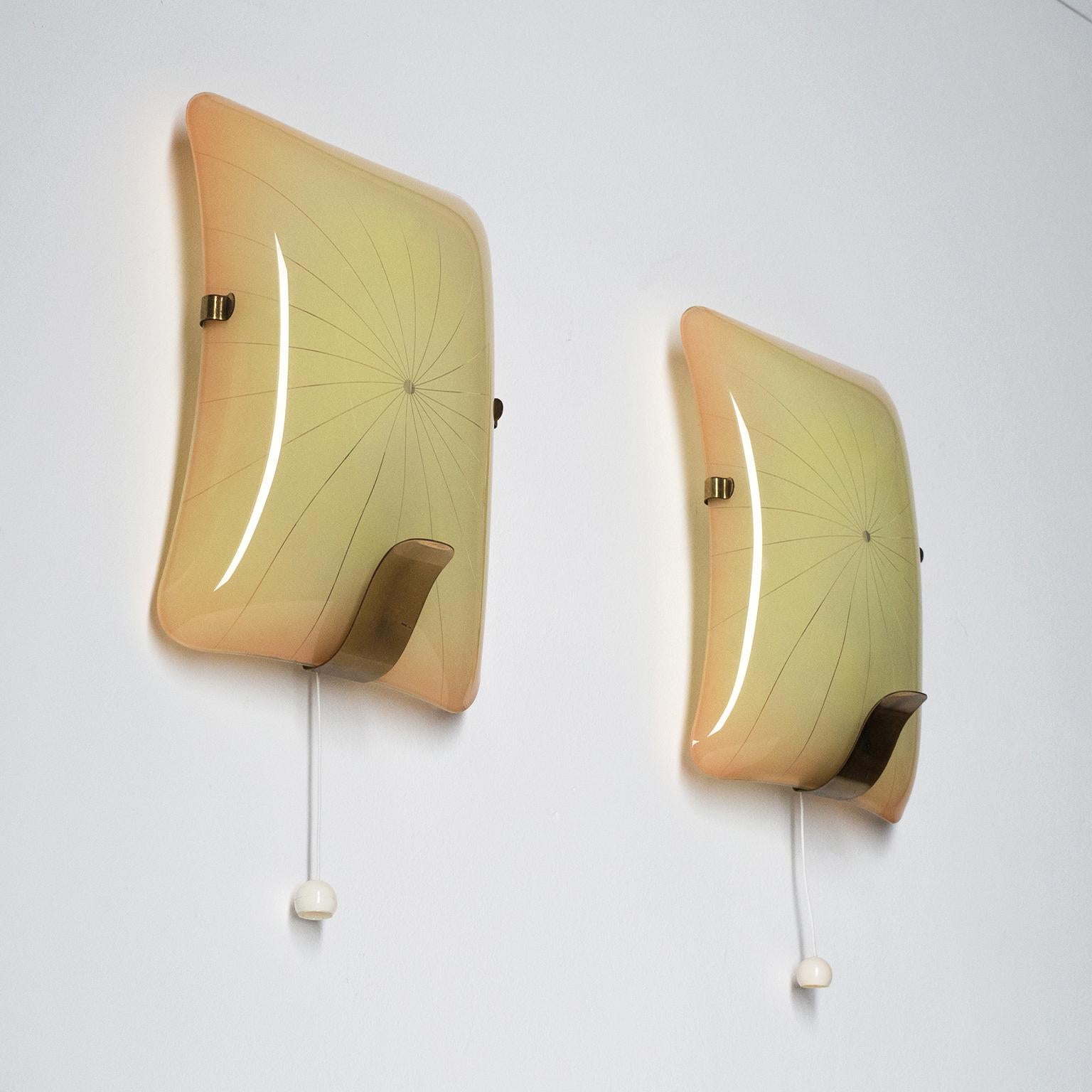 Rare pair of Art Deco sconces in enameled glass with brass details, 1940s. The curved rectangular glass with rounded edges is enameled on the backside with a gradient (going from cream in the center to peach on the edges) with radial and curved