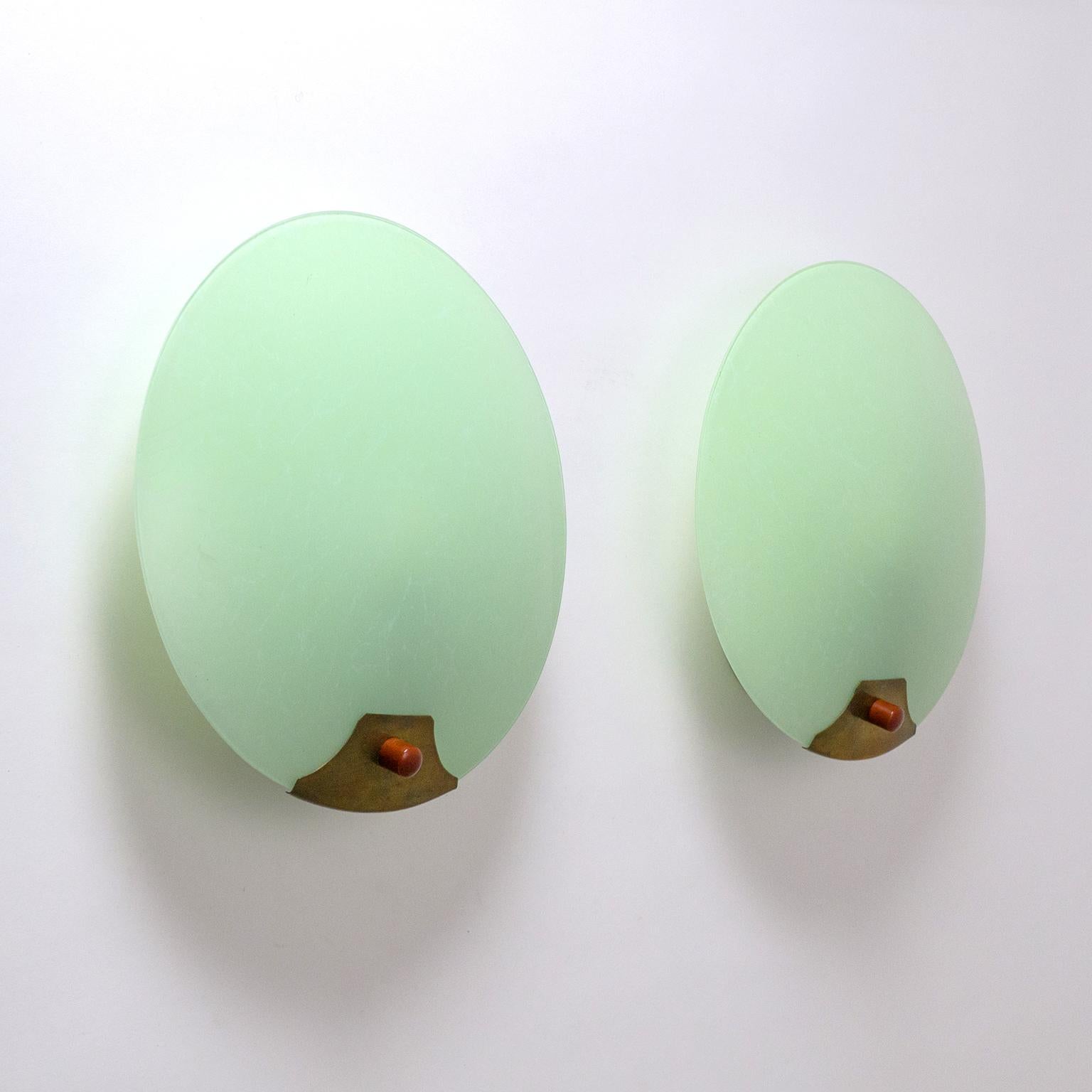 Very interesting pair of Art Deco wall lights, circa 1930. Slightly curved glass discs with a rear casing in mint with white streaks giving it a marbled effect. The glass is attached to the wall unit by a Bordeaux colored Bakelite knob with a pagoda