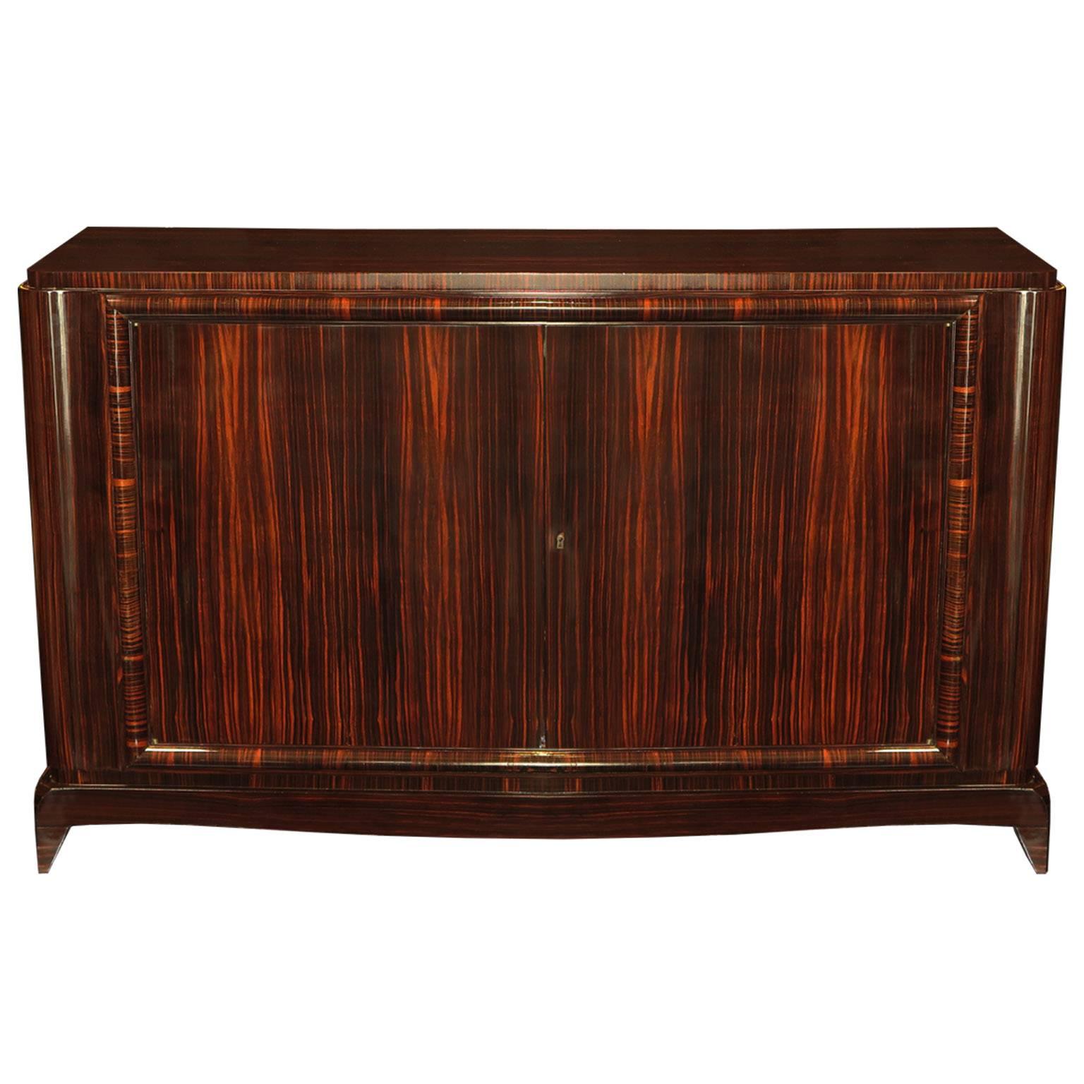 Classic pair of Art Deco sideboards exceptionally veneered in Macassar ebony. A rounded molding border decorates the outside of the ebony doors. A clean maple interior with two drawers and shelving for ample storage.