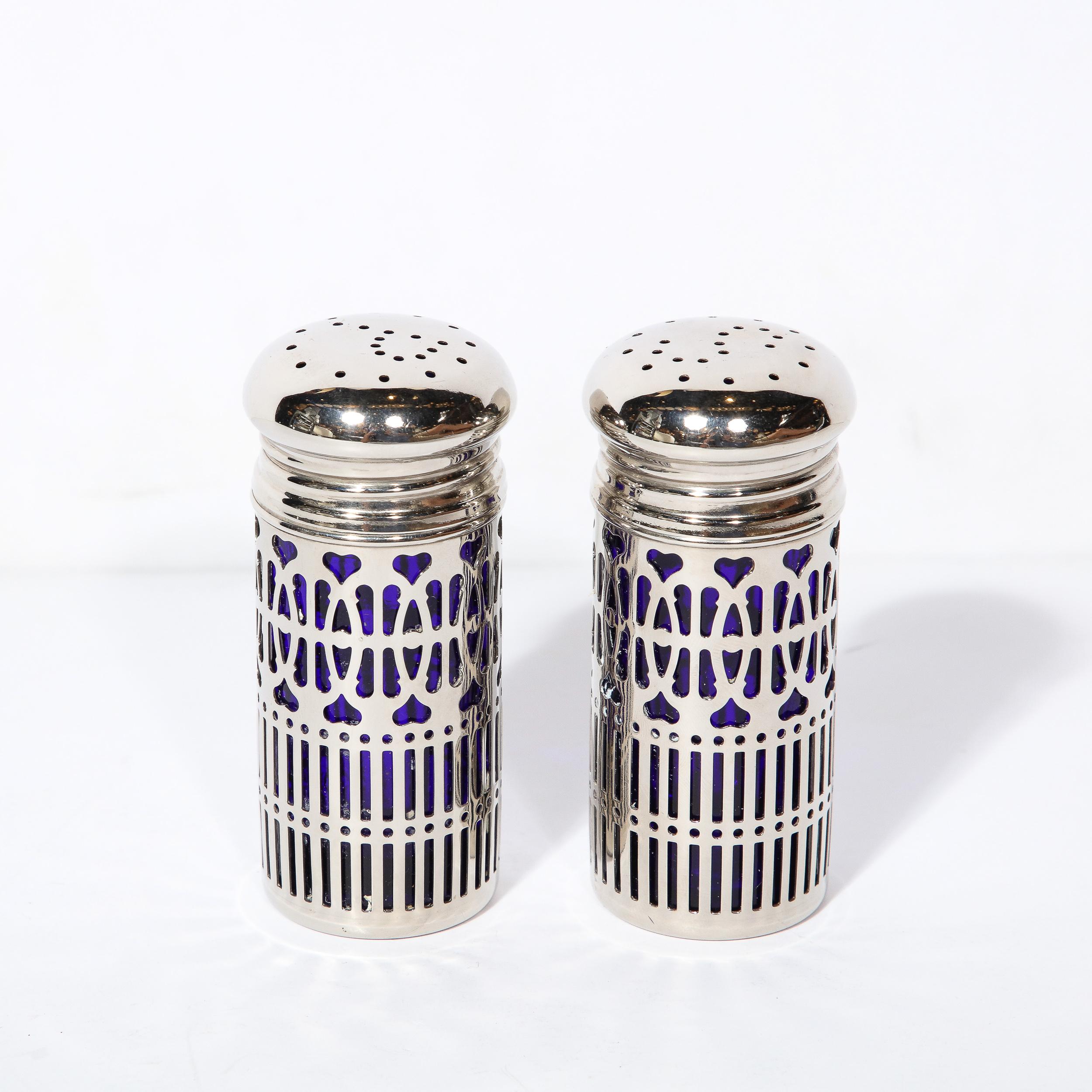 This pair of Art Deco Silver Plate and Cobalt Blue Glass Salt and Pepper Shakers originates from the United States during the 20th Century. Features beautiful geometric cut-out patterning consisting of looping arches and hearts resembling the
