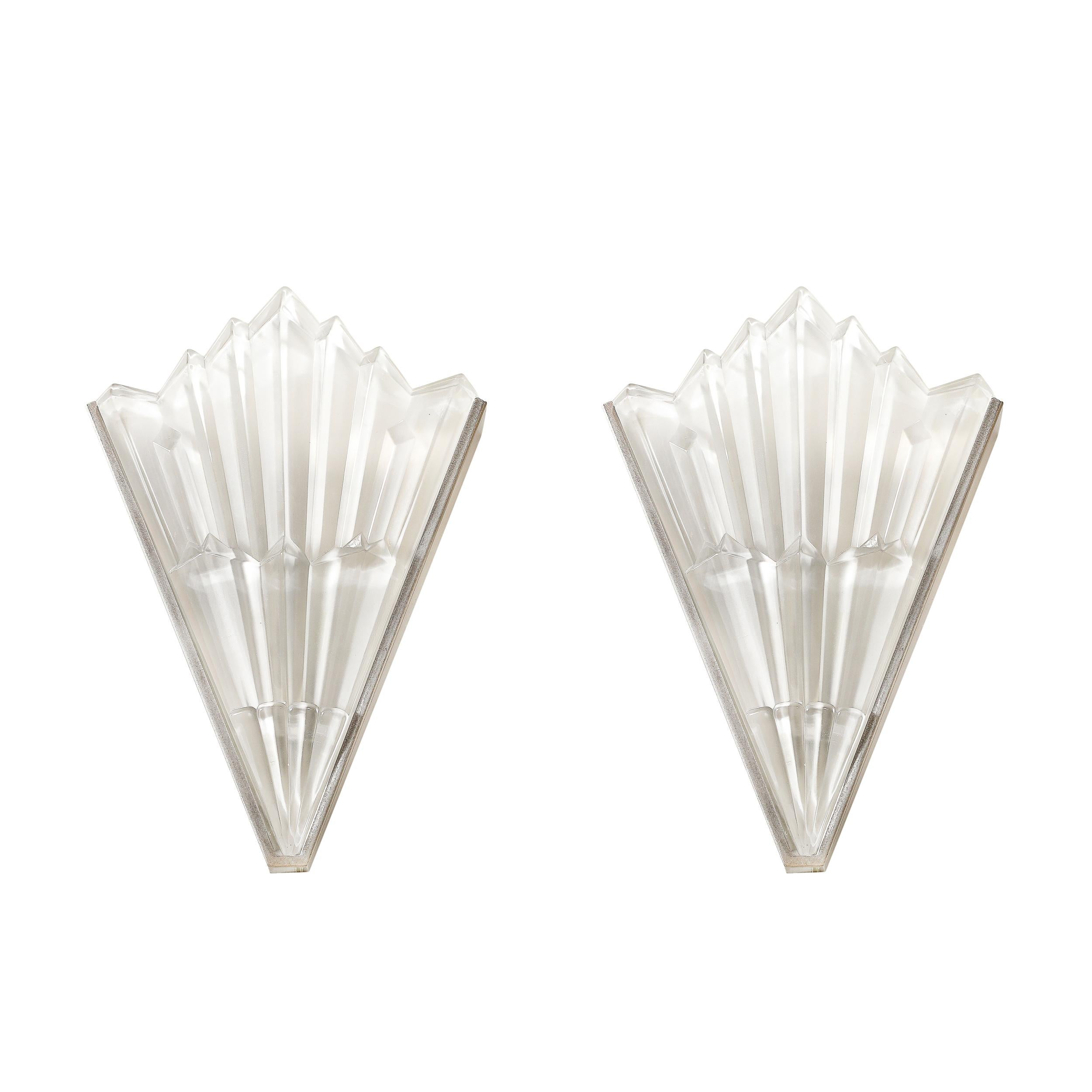 Questa splendida coppia di appliques Art Déco, risalente al 1930 circa, presenta un sorprendente design a grattacielo. I paralumi in vetro smerigliato sono realizzati con eleganza in forme geometriche a gradini, catturando l'essenza del movimento