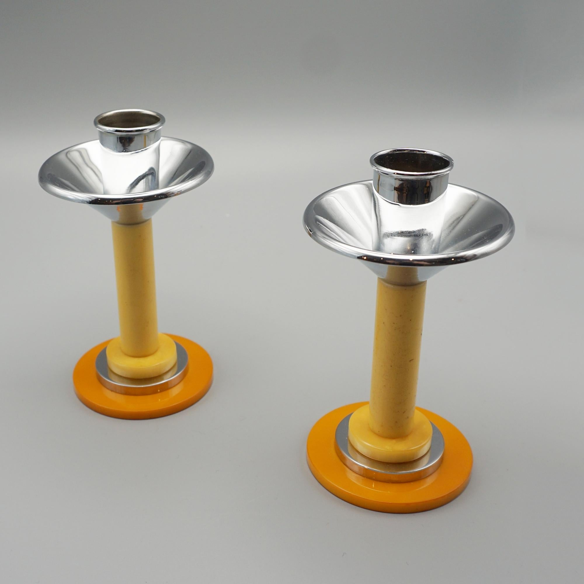 A Pair of Art Deco style candlesticks. Yellow bakelite stem over an orange bakelite base with chromed metal candle holders.

Dimensions: H 12cm D of Base 6cm 

