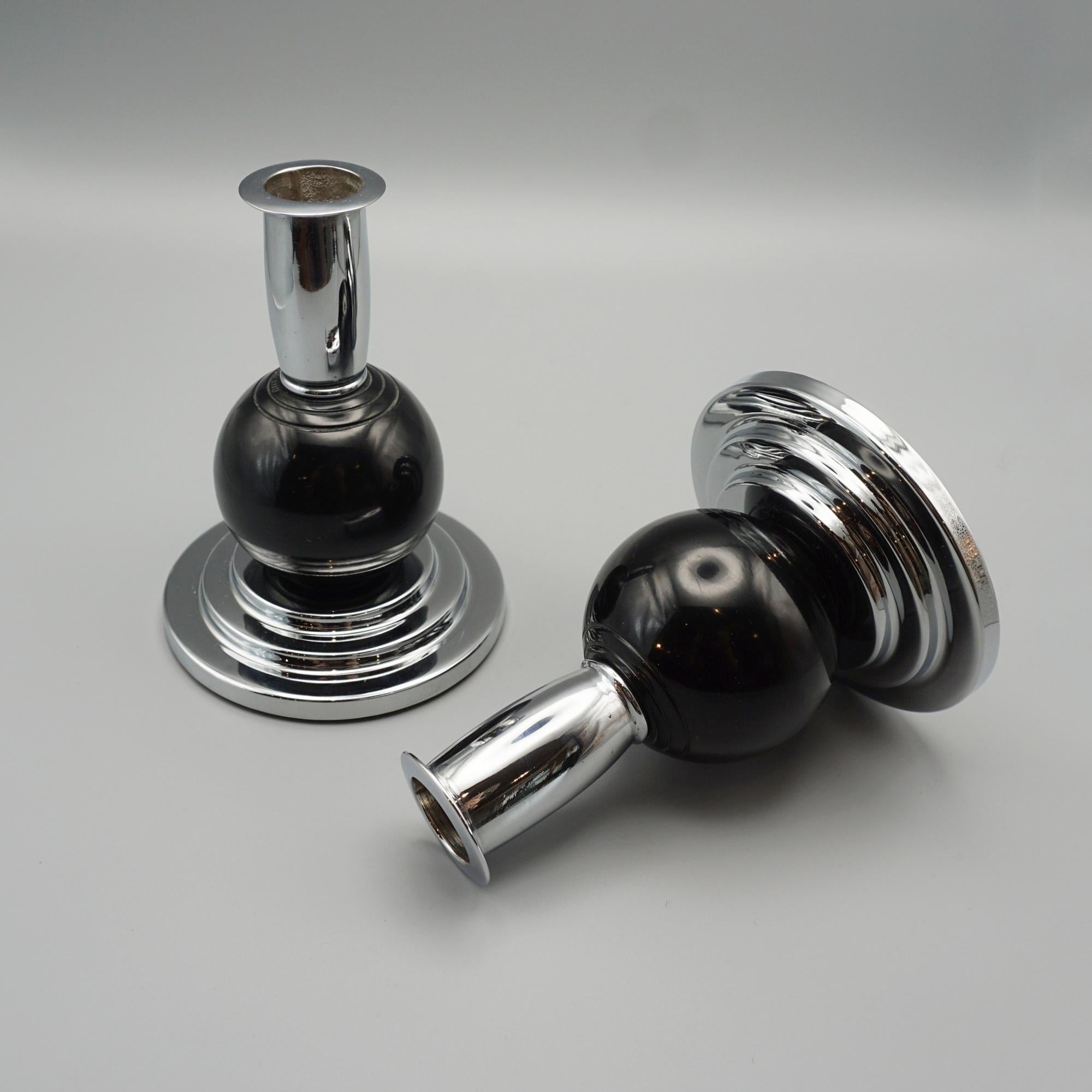 A Pair of Art Deco style candlesticks. A black bakelite stem set over a circular stepped base. 

Dimensions: H 13.5cm D of Base 10cm 

Re-chromed and polished with some replacement parts