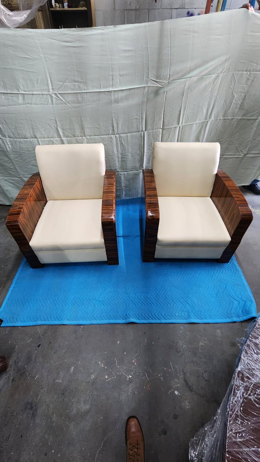 Questa inserzione presenta una coppia di sedie da salotto in stile Art Déco con braccioli in legno laccato a motivi e sedili imbottiti in pelle color crema, che pesano circa 70 libbre ciascuna.