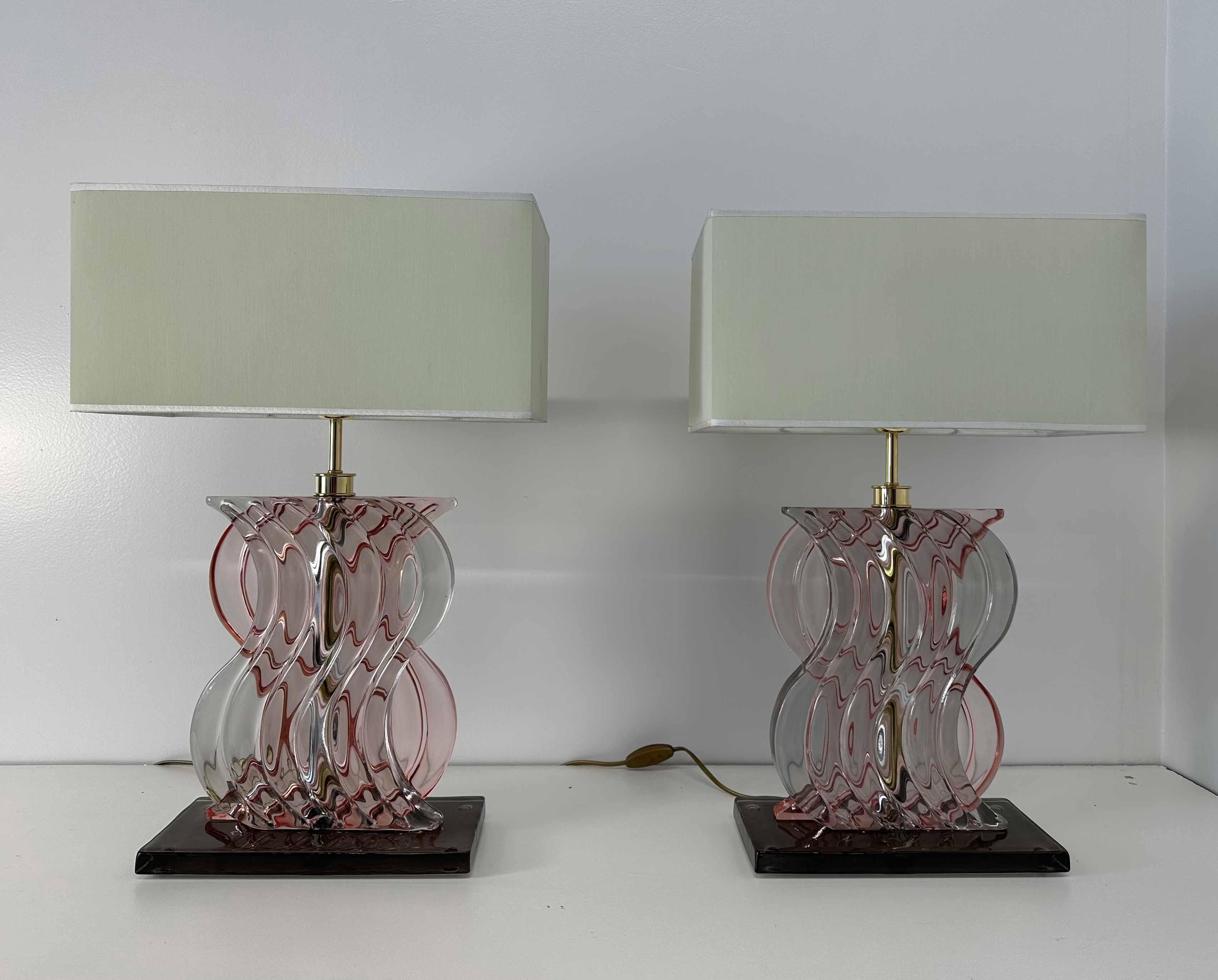 This pair of Art Deco Style lamps was produced in Italy in the 2000s. 
The central part of the structure is in gold galvanized brass, covered with a pastel pink sinuous Murano glass. The base is a brown piece of Murano glass. 
The lampshade is