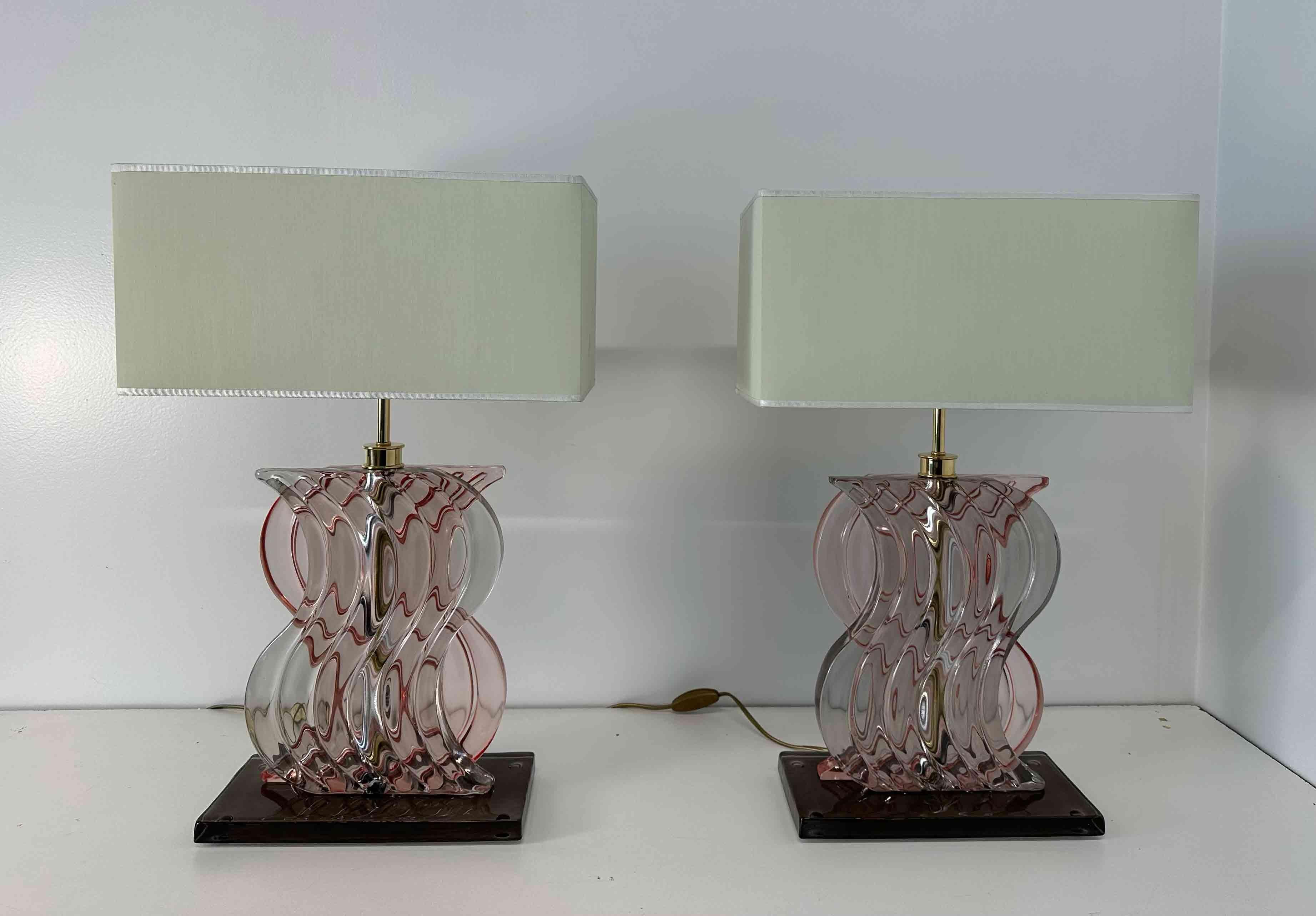 Esta pareja de lámparas de estilo Art Déco se fabricó en Italia en la década de 2000. 
La parte central de la estructura es de latón galvanizado dorado, recubierto de un sinuoso cristal de Murano rosa pastel. La base es una pieza marrón de cristal
