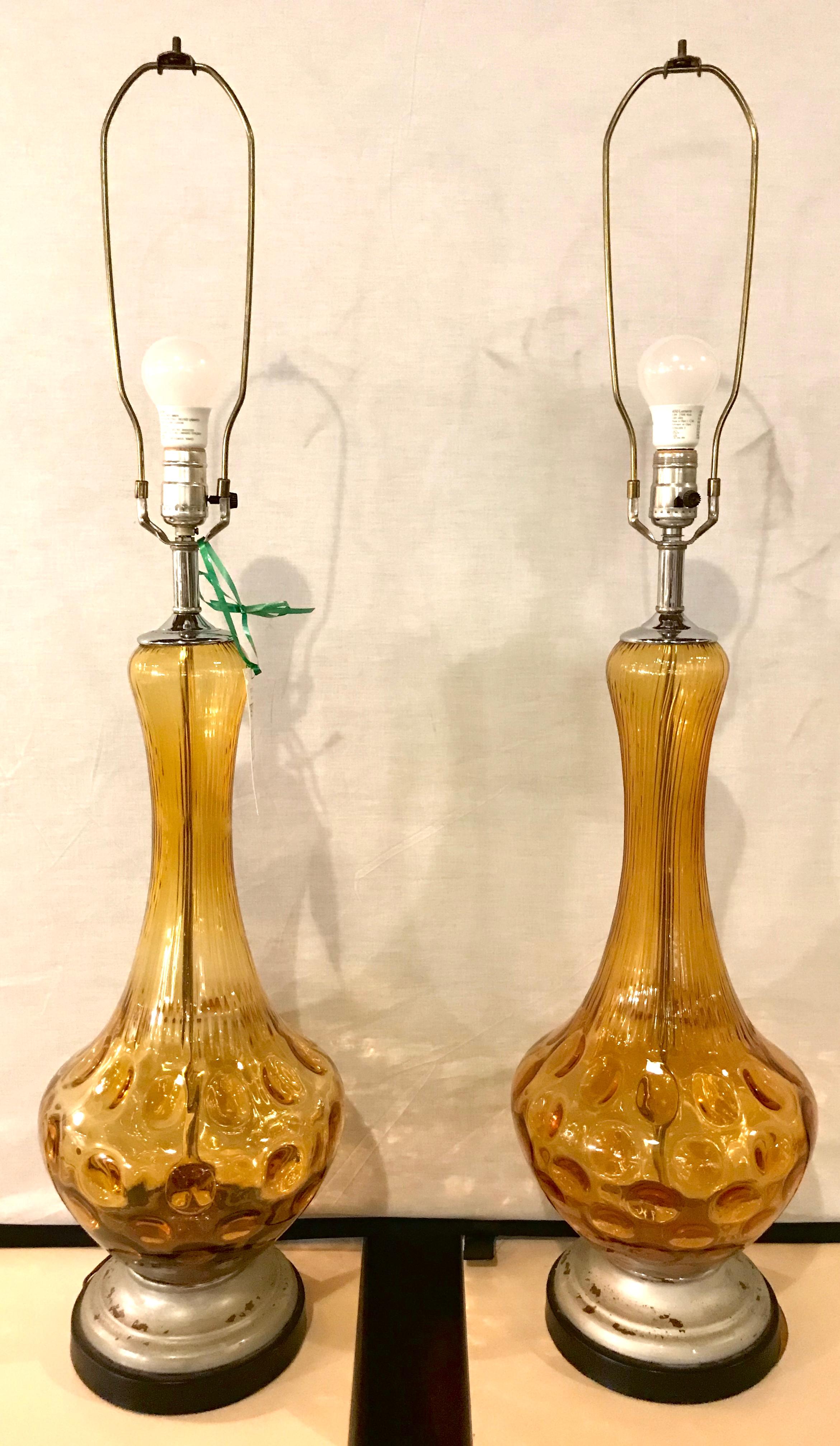 Pair of Art Deco style sculpted amber glass lamps. The pair on a silver gilt and ebony wooden base.