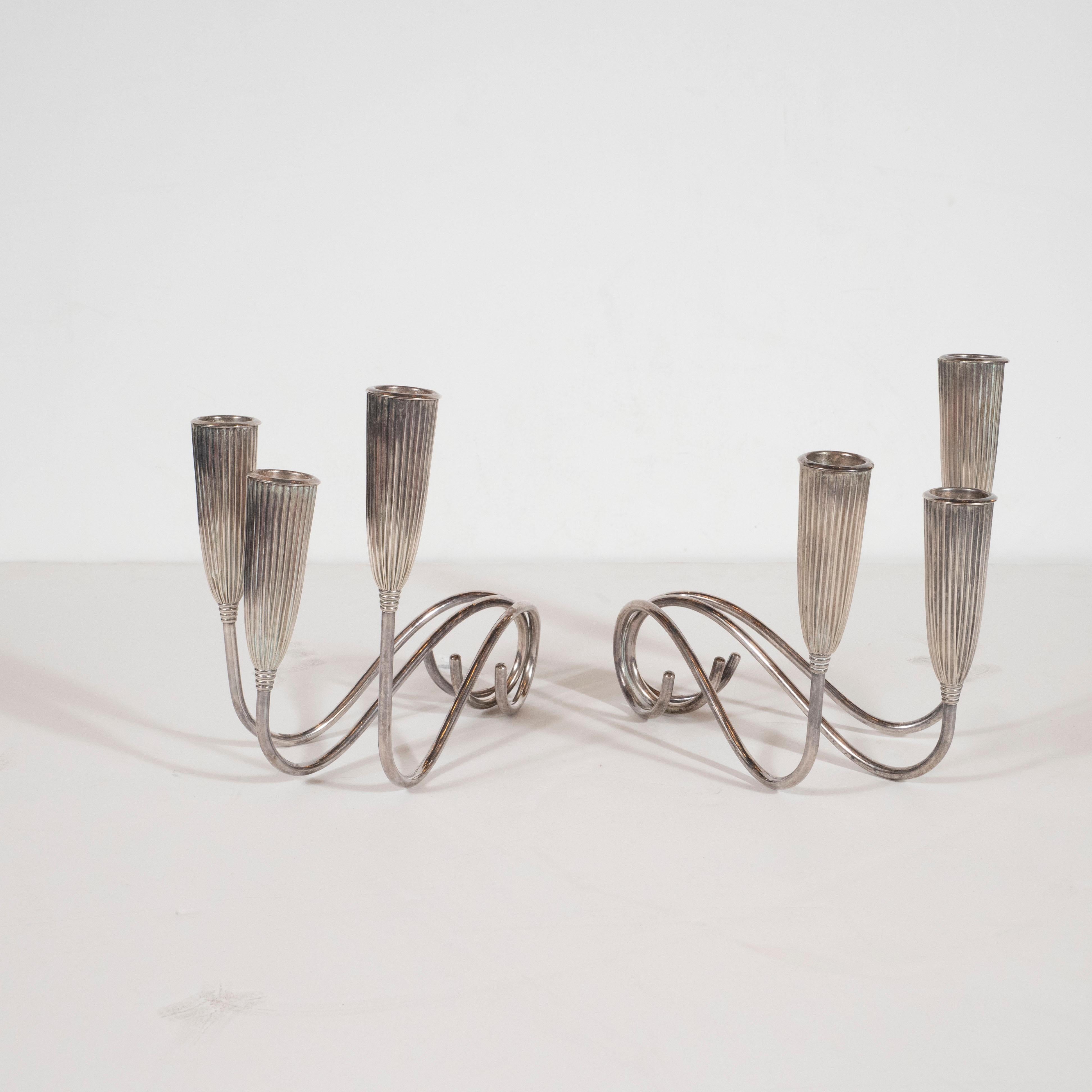 This elegant and graphic pair of silver plated triple branch candlesticks were realized by the celebrated design firm Napier Co., in the United States, circa 1940. Each features three undulating arms that culminate in fluted bullet form supports.