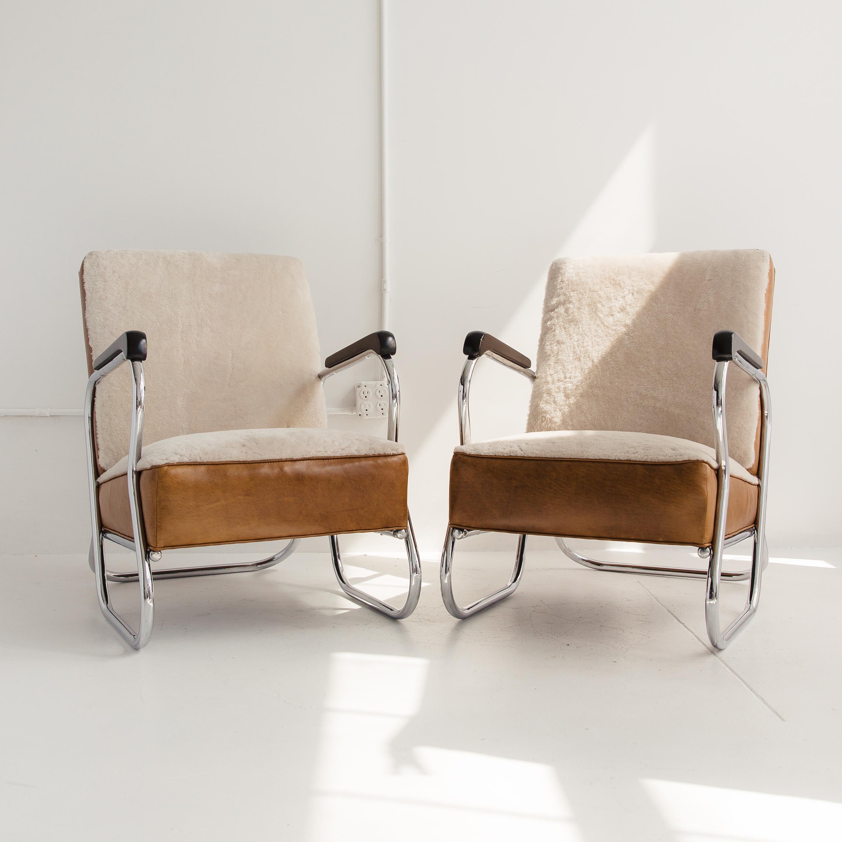 A handsome pair of Art Deco lounge chairs featuring a tubular, polished chrome frame, ebonized wood armrests and an upholstered seat. The chair was recently reupholstered with a white shearling seat and contrasting cognac leather sides. As