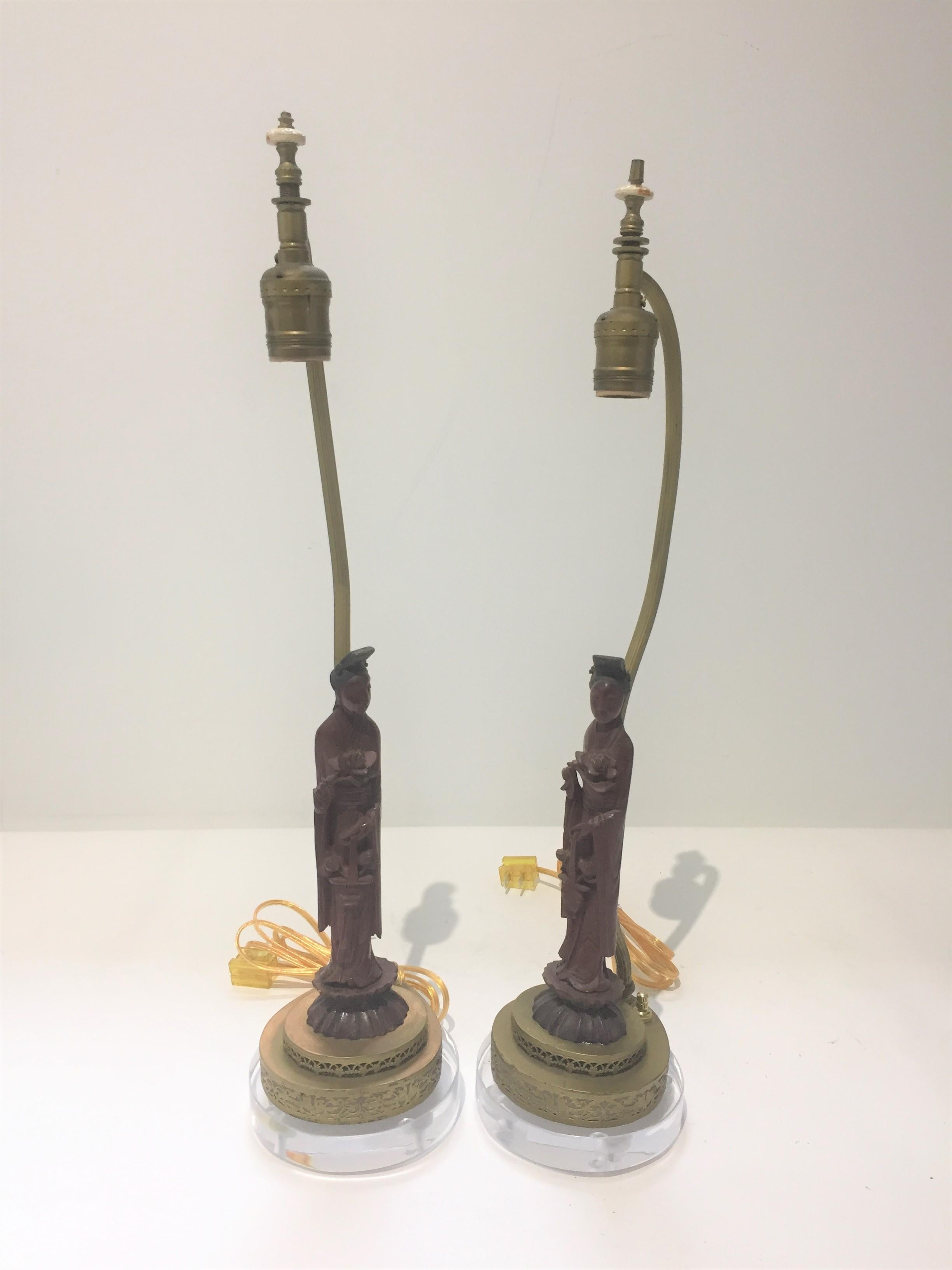 This stylish pair of Art Deco vanity table lamps date to the 1920s thru the 1930s and are fabricated with dark cinnabar colored Quan Yin figures holding a lotus flower.

These have recently been re-wired and mounted on Lucite bases.

Over time