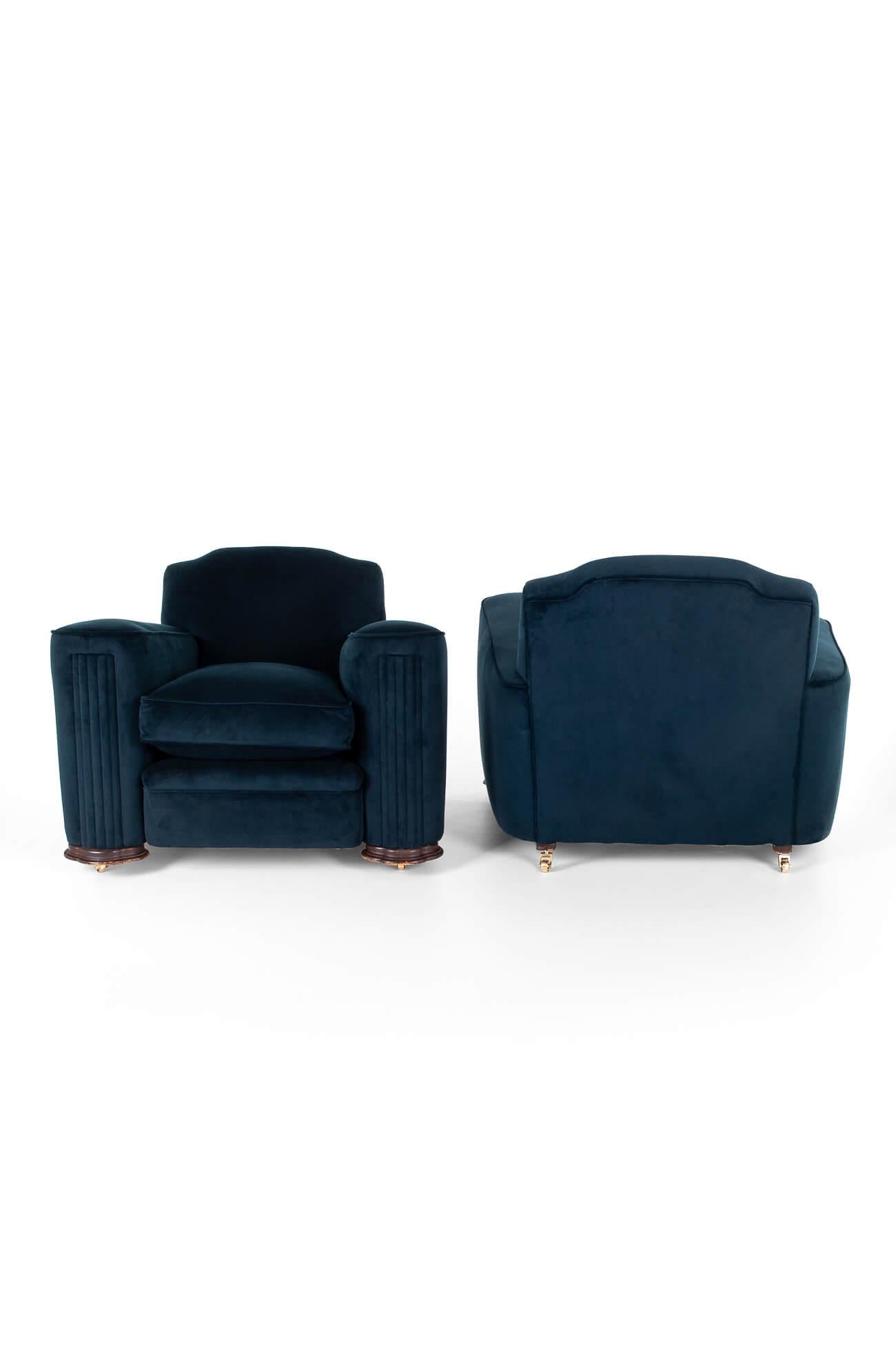 A commanding matching pair of Art Deco lounge chairs in a rich navy blue upholstery.

The armchairs have high backs and large shapely column arms with pleated fronts that surround the generous seats. Both chairs are raised on oak feet and finished
