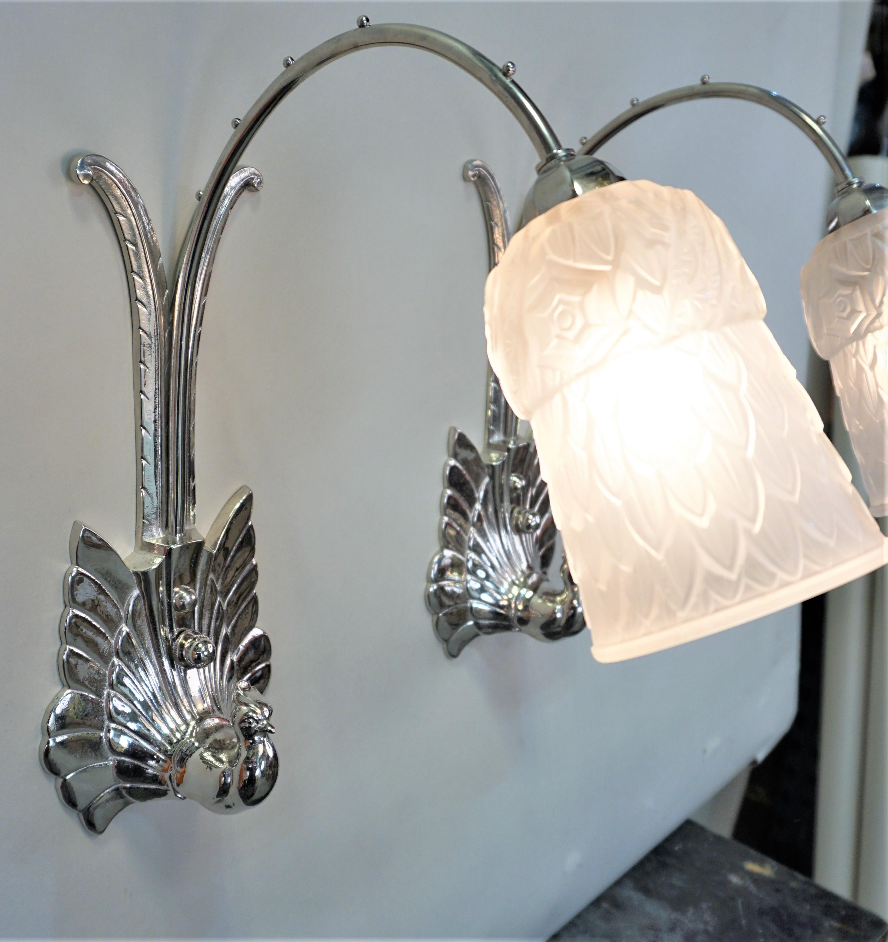 Elegant pair of 1930 French Art Deco wall sconces in nickel on bronze bird holding clear frost glass shades.