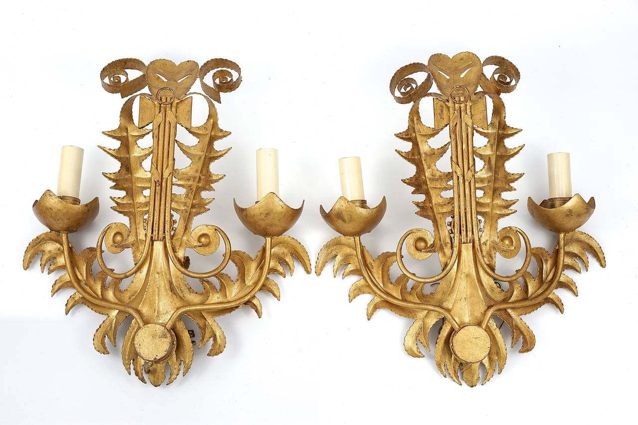Pair of stylish, chic and dramatic French, Art Deco style wall sconces are detailed with stylized acanthus leaves, arrow quiver with crossbanding, floral medallions and theatrical masks with flowing ribbons. 

Note: The candle sleeves are paper