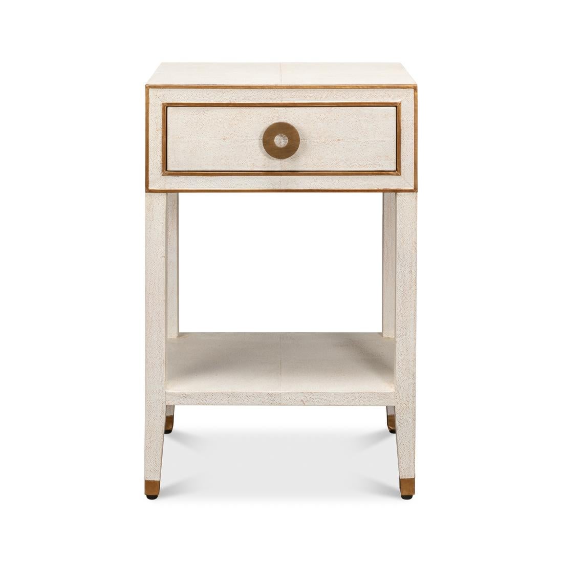 La table de nuit blanche associe des surfaces blanches Osprey sophistiquées à texture de galuchat et des accents dorés pour une déclaration de luxe vintage. La façade détaillée présente des garnitures géométriques en laiton et une tirette circulaire