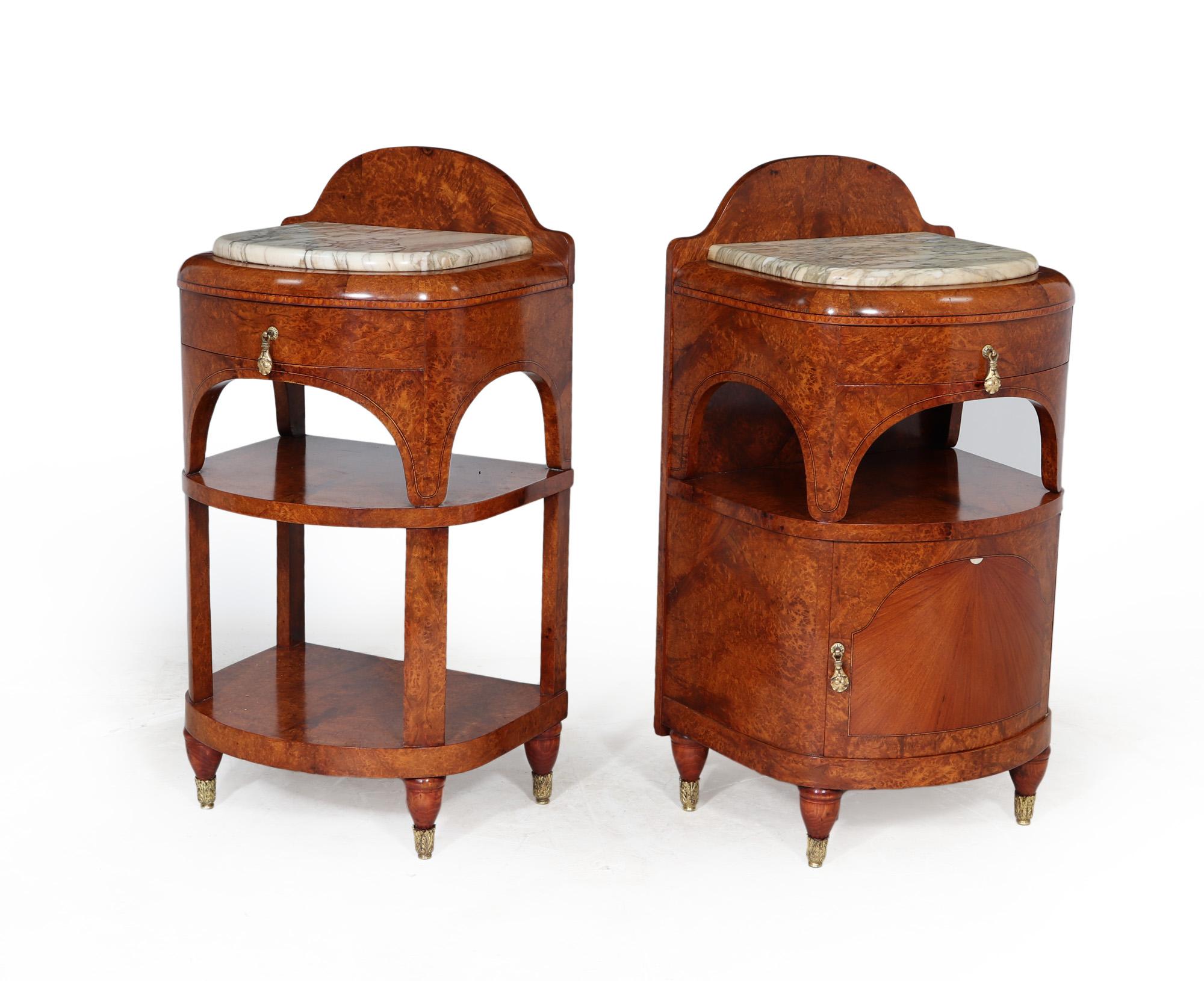 A pair of French Art Nouveau bedside cabinets of two different forms one having a cupboard shelf and drawer and the other with shelves and drawer, both are amboyna with inlaid detail and having an upstanding back with thick rounded corner white