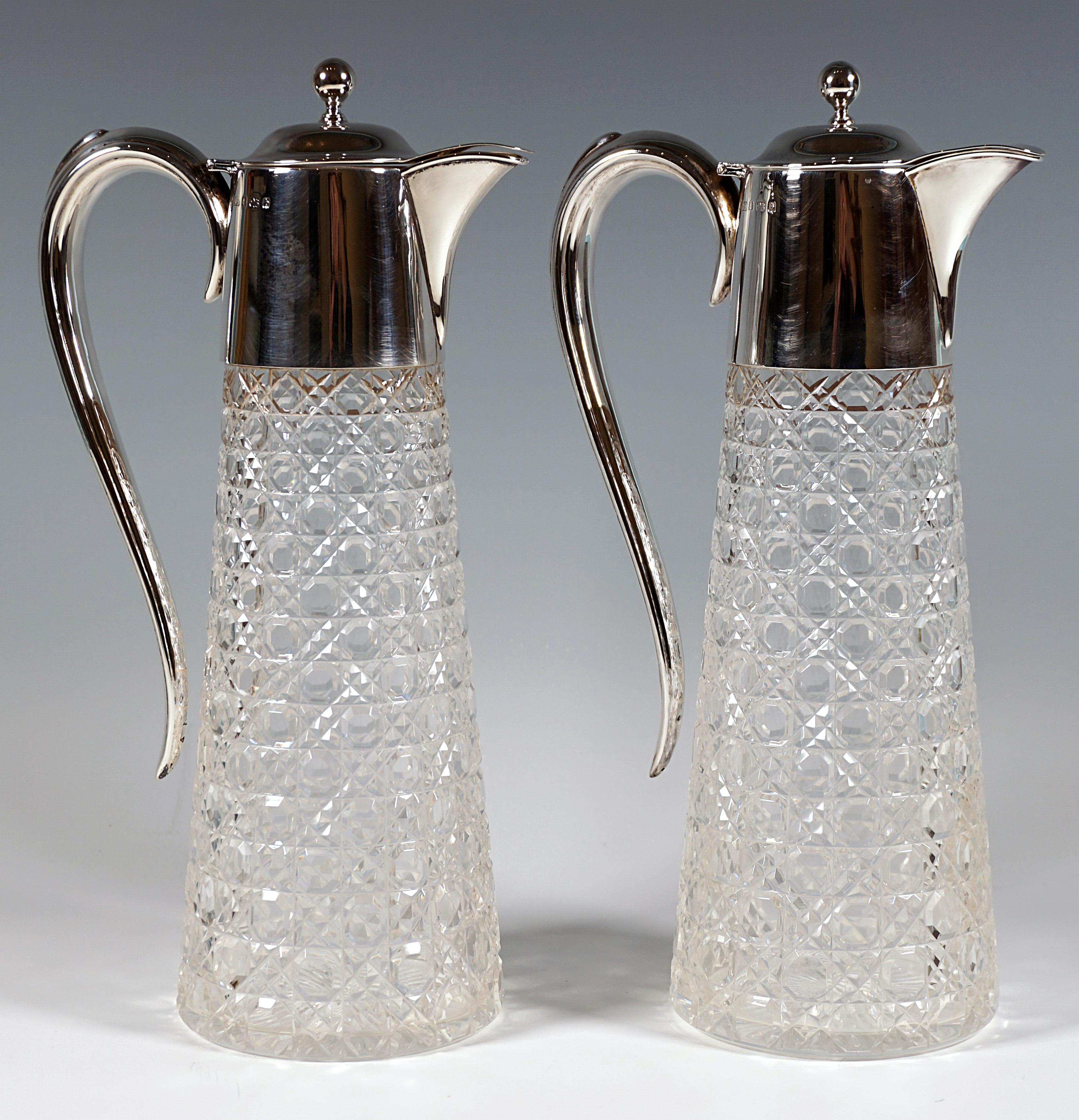 Two Edward VII clear glass carafes with a conical body, elaborate steinel and octagonal cut on the outer wall, finely radiated base star, smooth silver mount with beak spout and elegantly curved handle, hinged slightly domed lid with curved spout