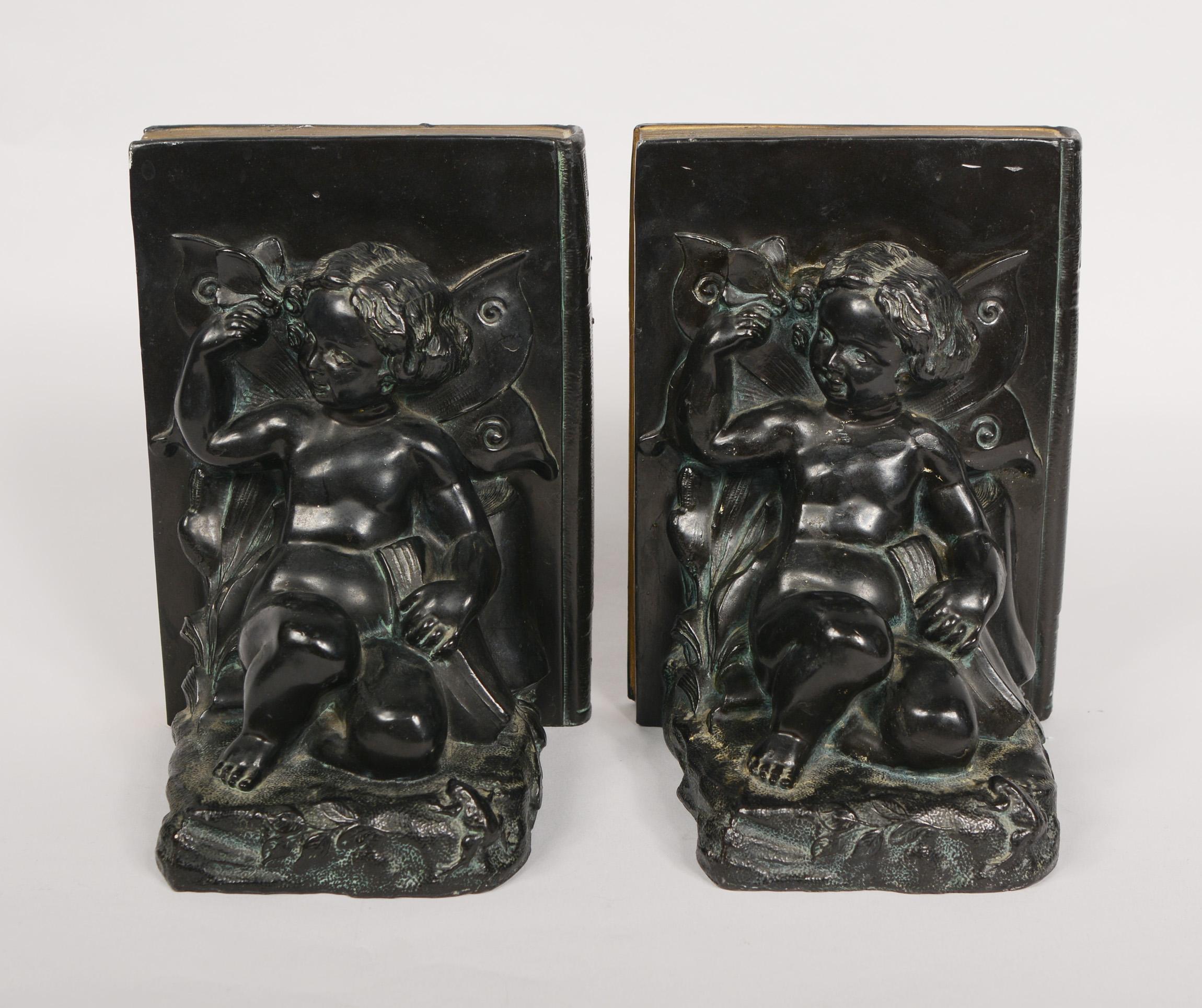Pair of white metal bookends by Ronson Art Metal Works. These have a cherub with butterfly wings. She is holding a butterfly in one hand and a book in the other. There is a frog looking up at her. These are art nouveau in style with a art deco