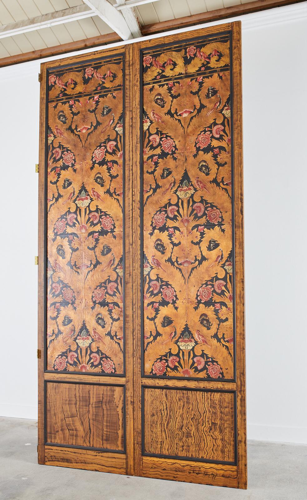 Extraordinary pair of massive art nouveau leather inset panel screens featuring flora and fauna embossed and painted designs. The leather panels are decorated with birds, squirrels, and mythical beasts amid gilt foliage and red floral blooms. The
