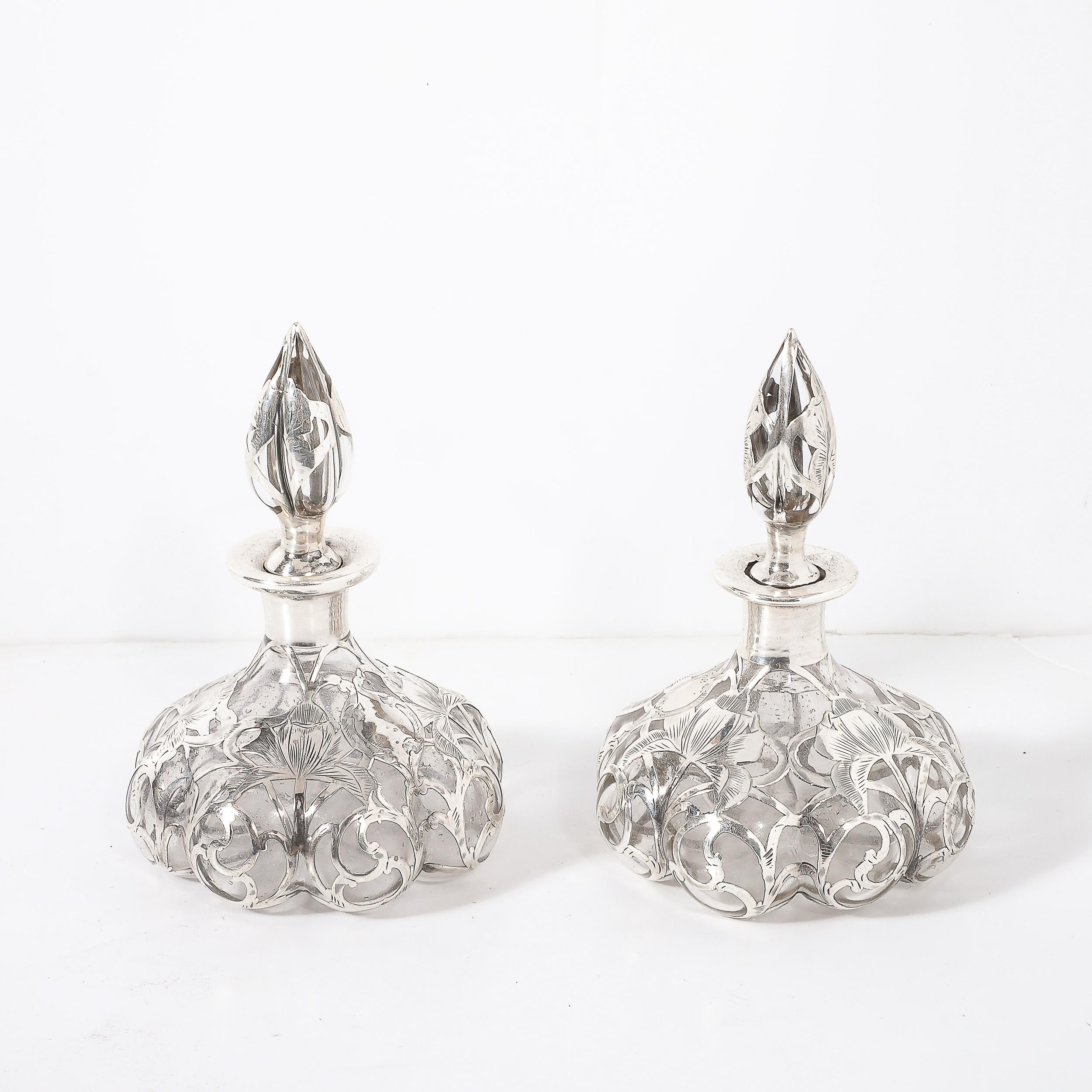 Questa raffinata coppia di flaconi di profumo Art Nouveau, realizzati dalla stimata Steuben Glass Company intorno al 1910, esemplifica l'eleganza e l'innovazione del periodo. Ogni bottiglia presenta un lussuoso rivestimento in argento sterling,